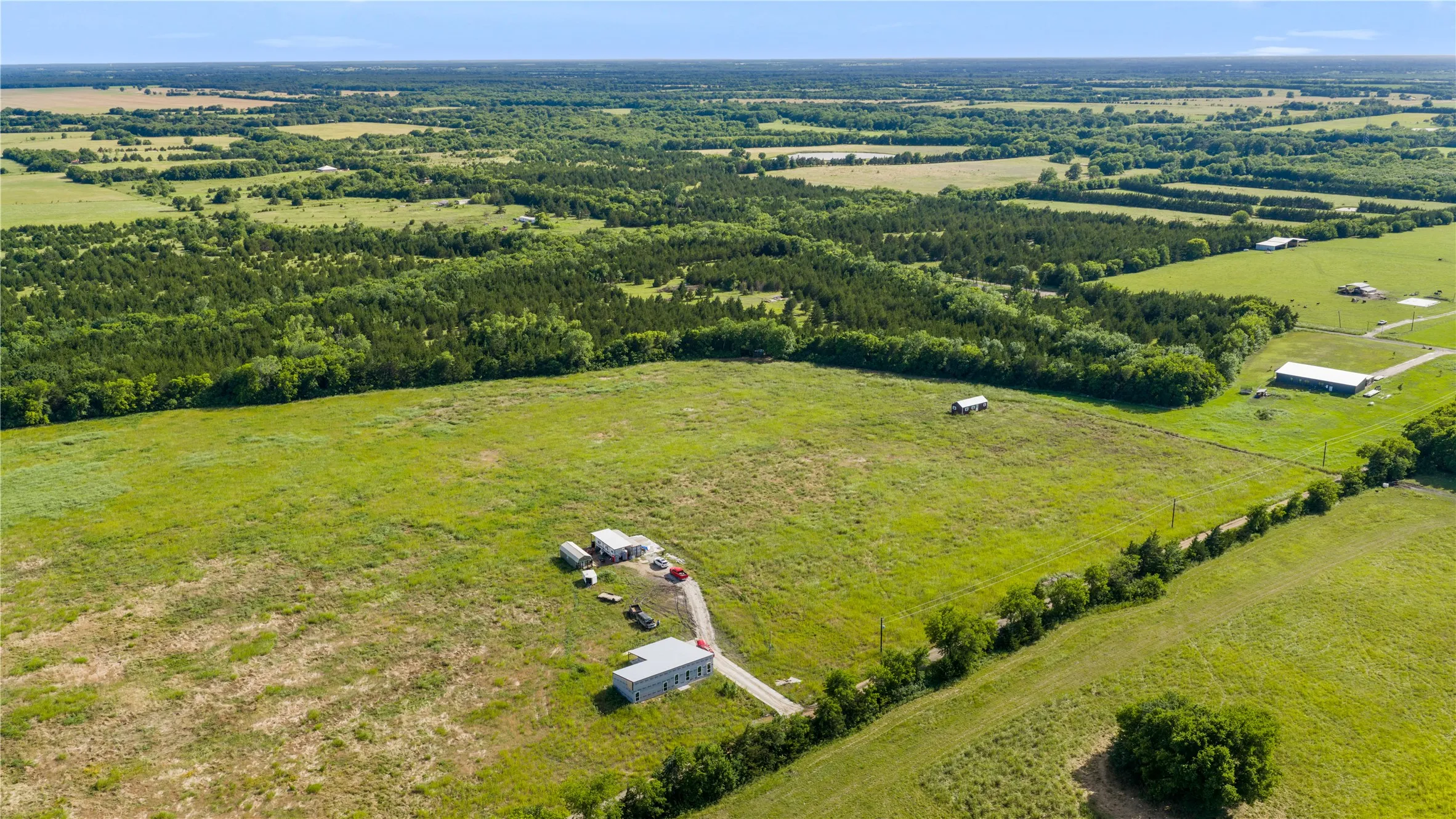 Expansive rural property featuring a large open field, several structures, and a gravel driveway