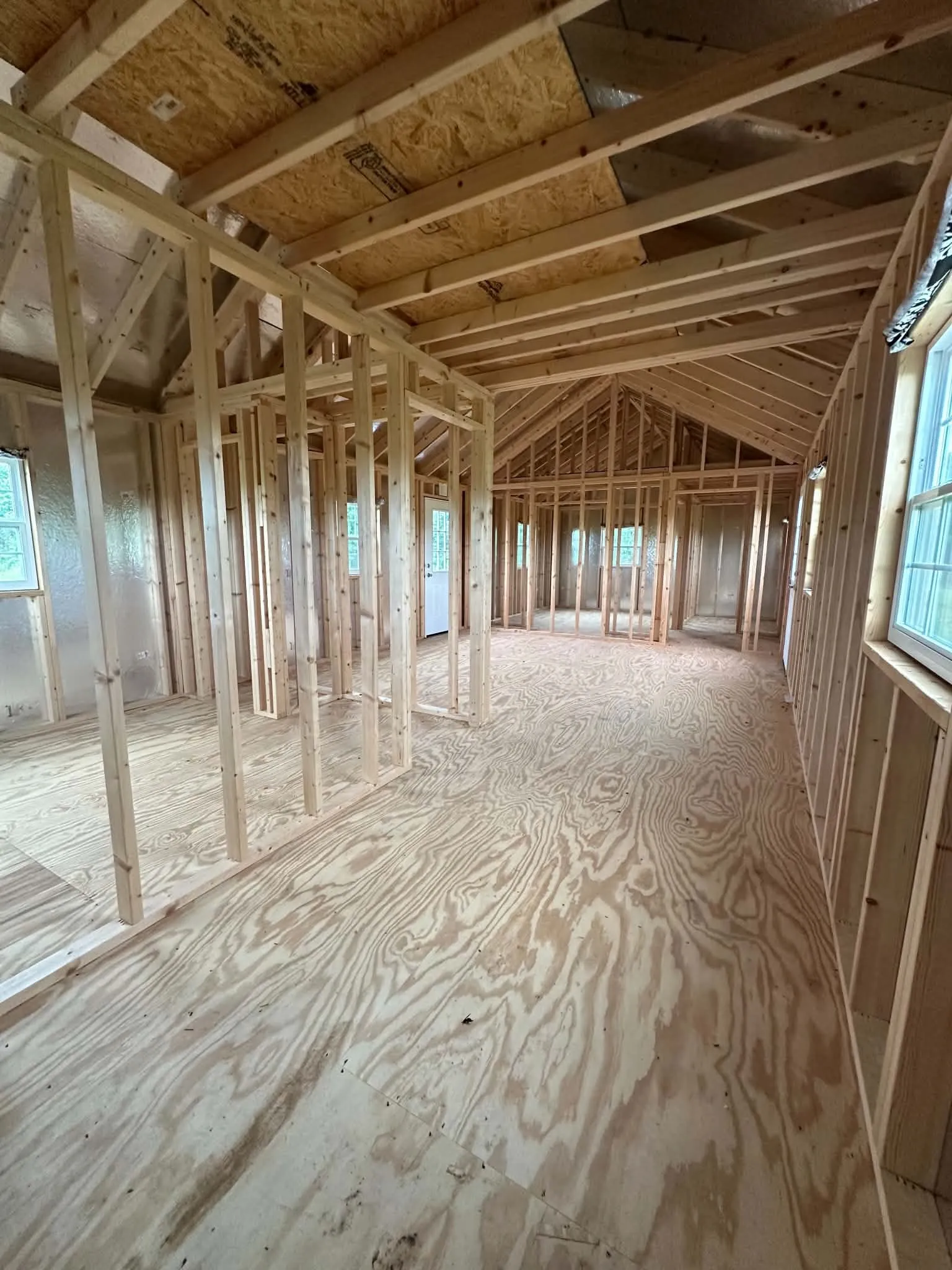 Interior framing showcasing exposed wood studs, plywood subflooring, and a vaulted ceiling with exposed rafters