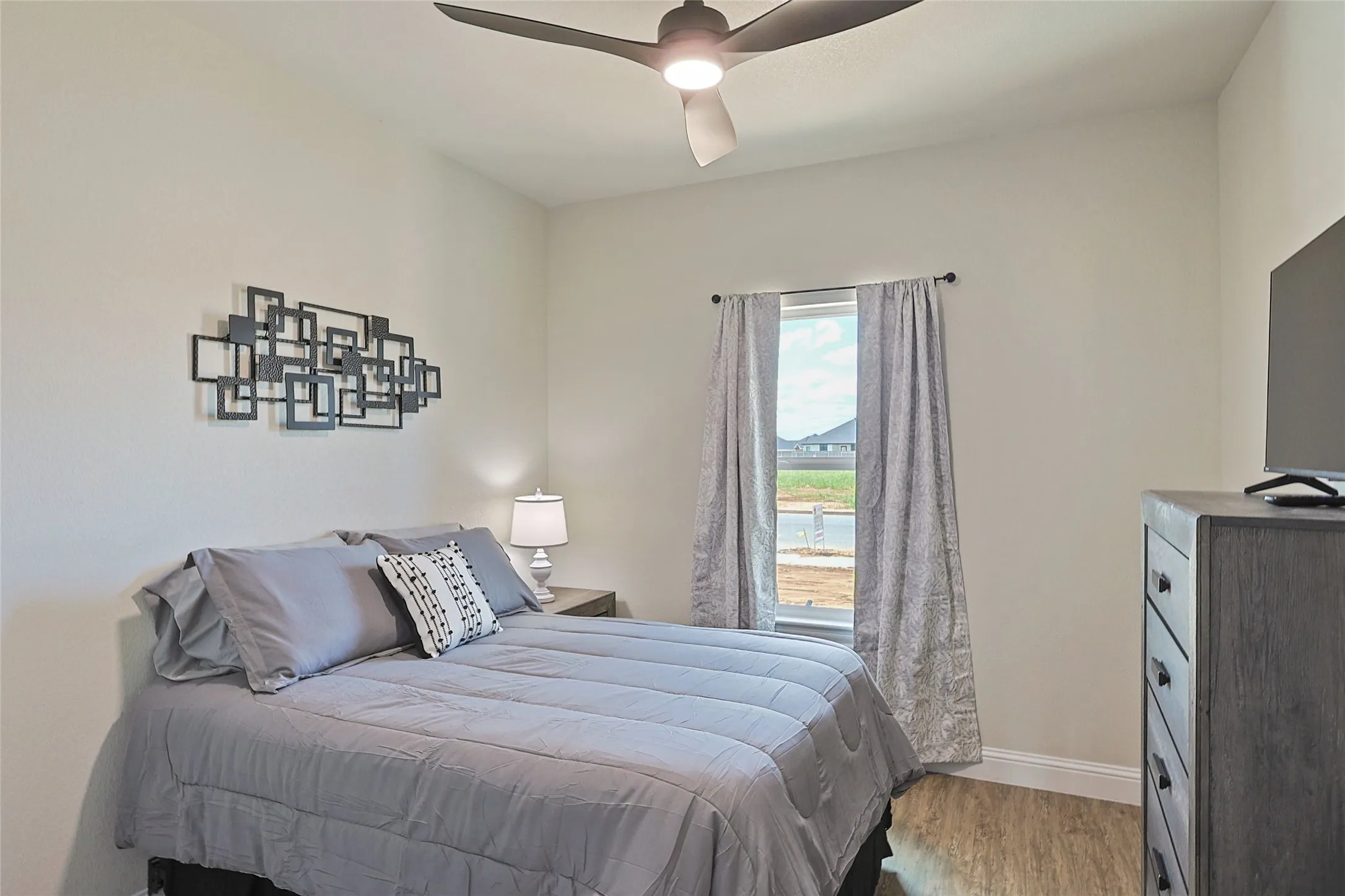 Bedroom featuring light neutral wall paint, a ceiling fan with integrated lighting, a single window, and wood-finish flooring