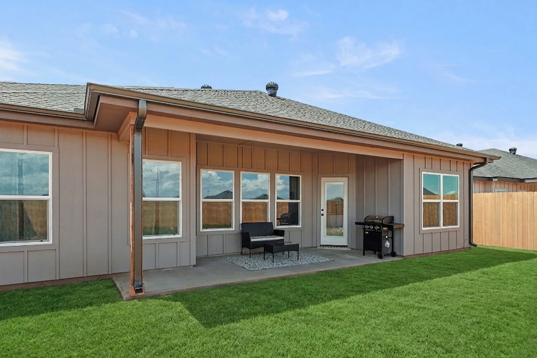 Expansive backyard featuring a covered patio, multiple windows, and a manicured lawn