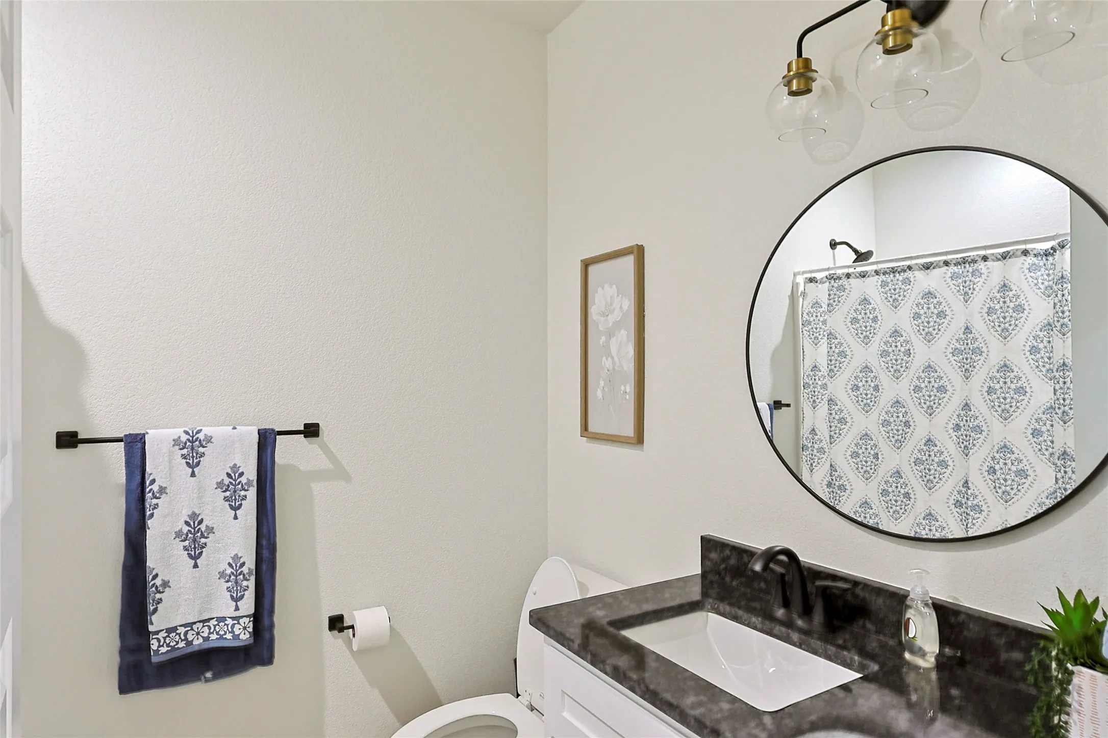 Bathroom featuring a dark countertop vanity with an integrated sink, a circular black-framed mirror, and a modern three-light fixture