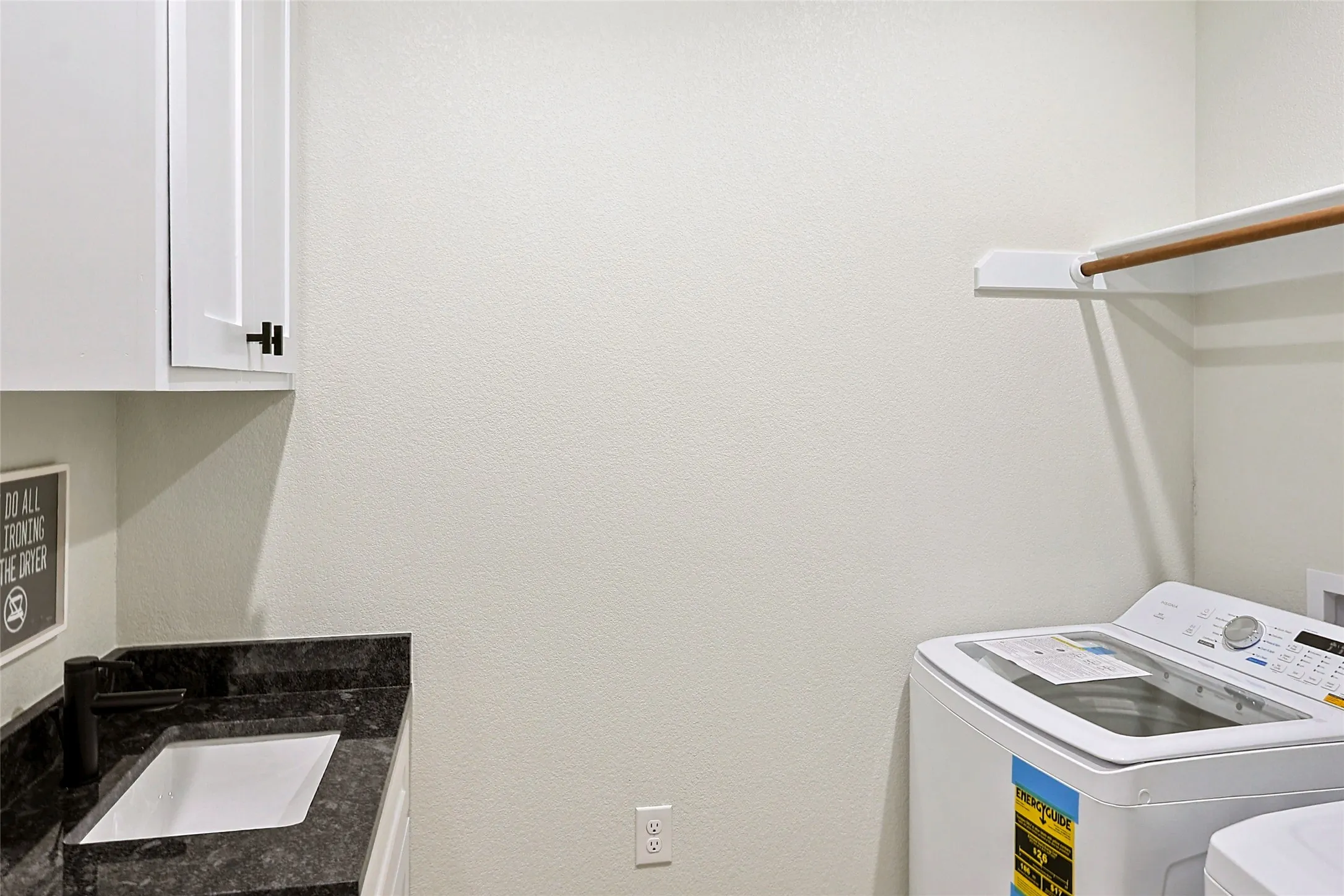 Laundry room featuring white cabinetry, a dark countertop with an undermount sink, a matte black faucet, and a wall-mounted hanging rod