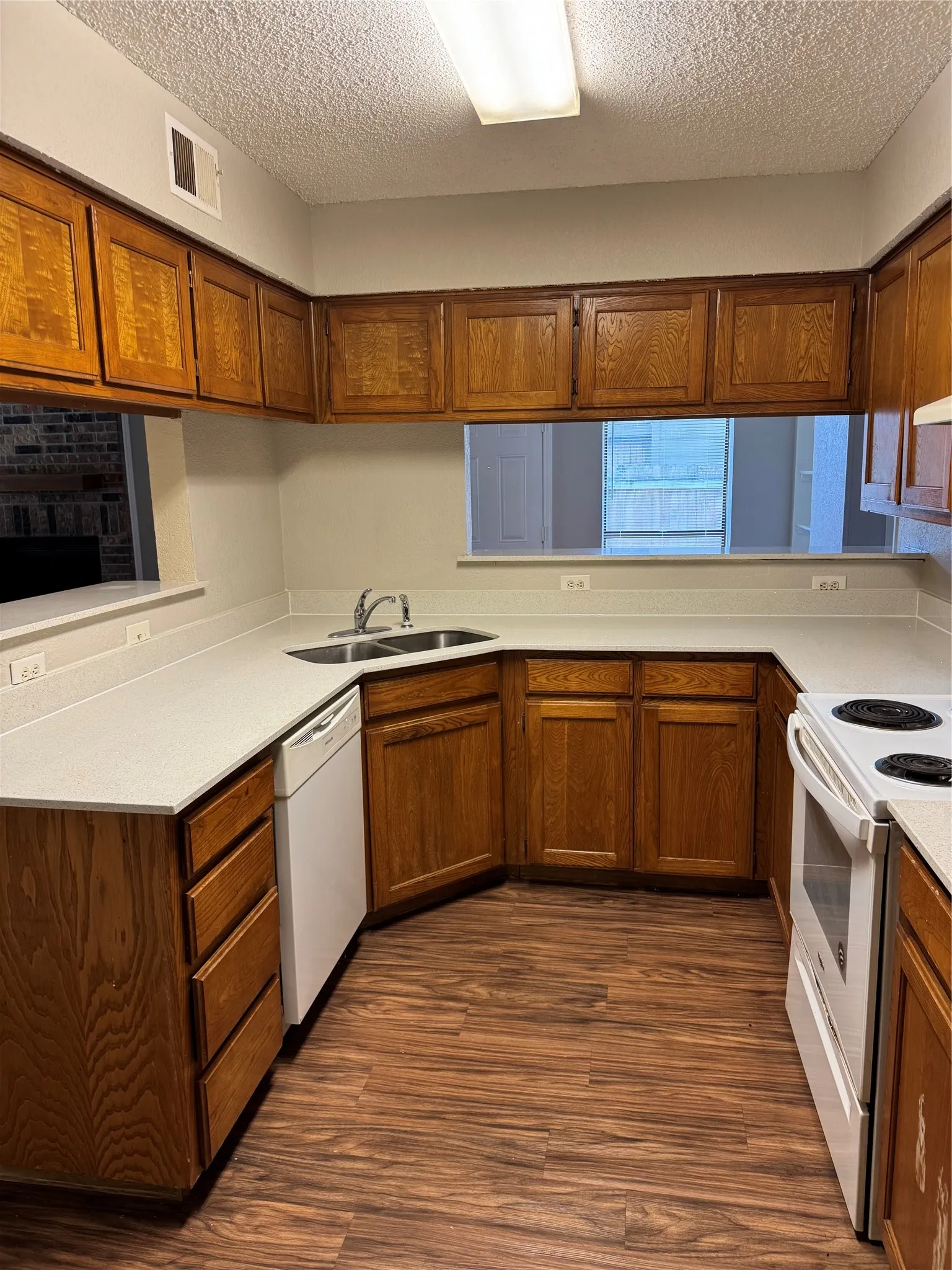 U-shaped kitchen featuring wood cabinetry, light-toned countertops, a double basin sink with a chrome faucet, and wood-finish flooring
