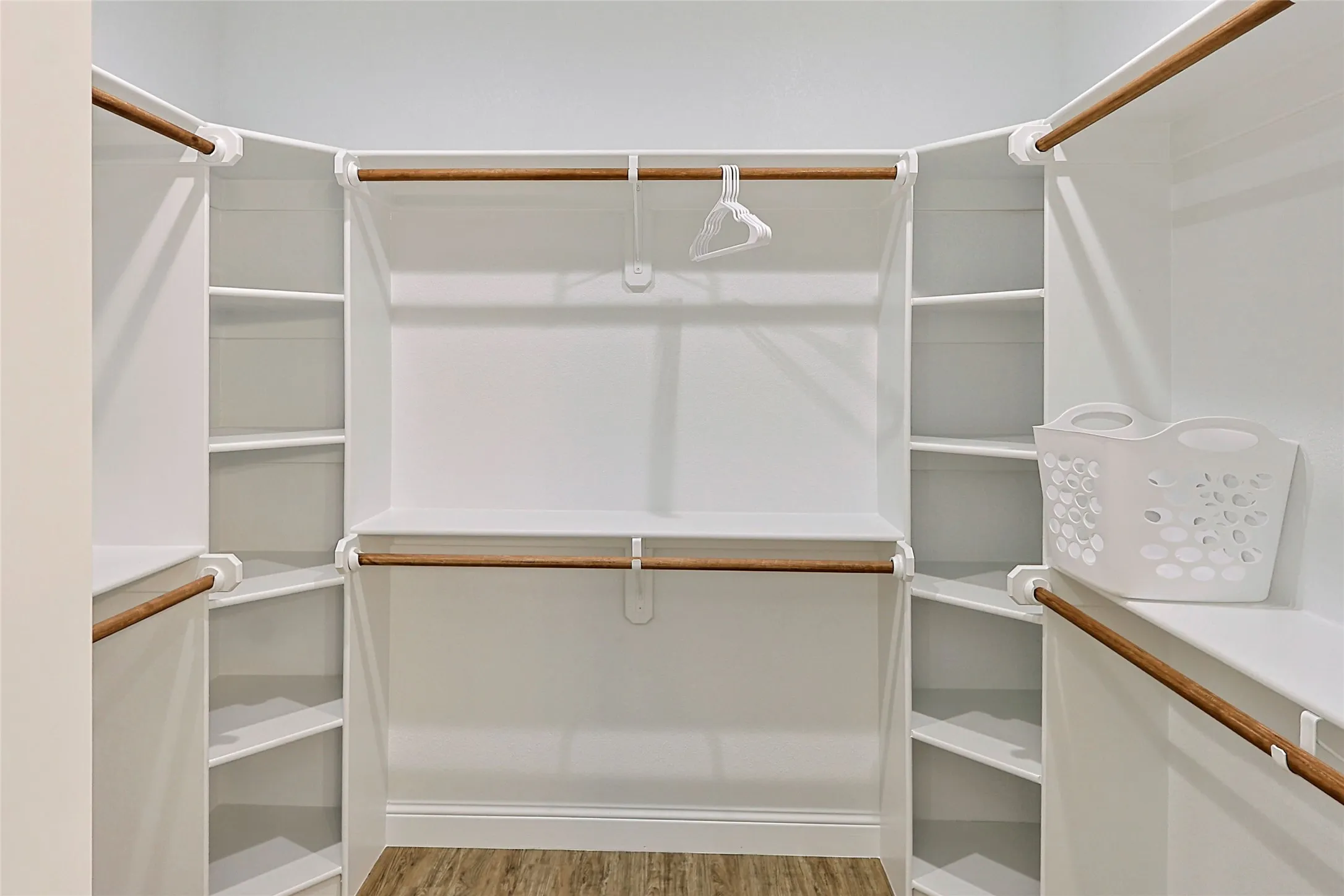 Spacious walk-in closet featuring white built-in shelving, multiple hanging rods, and wood-finish flooring