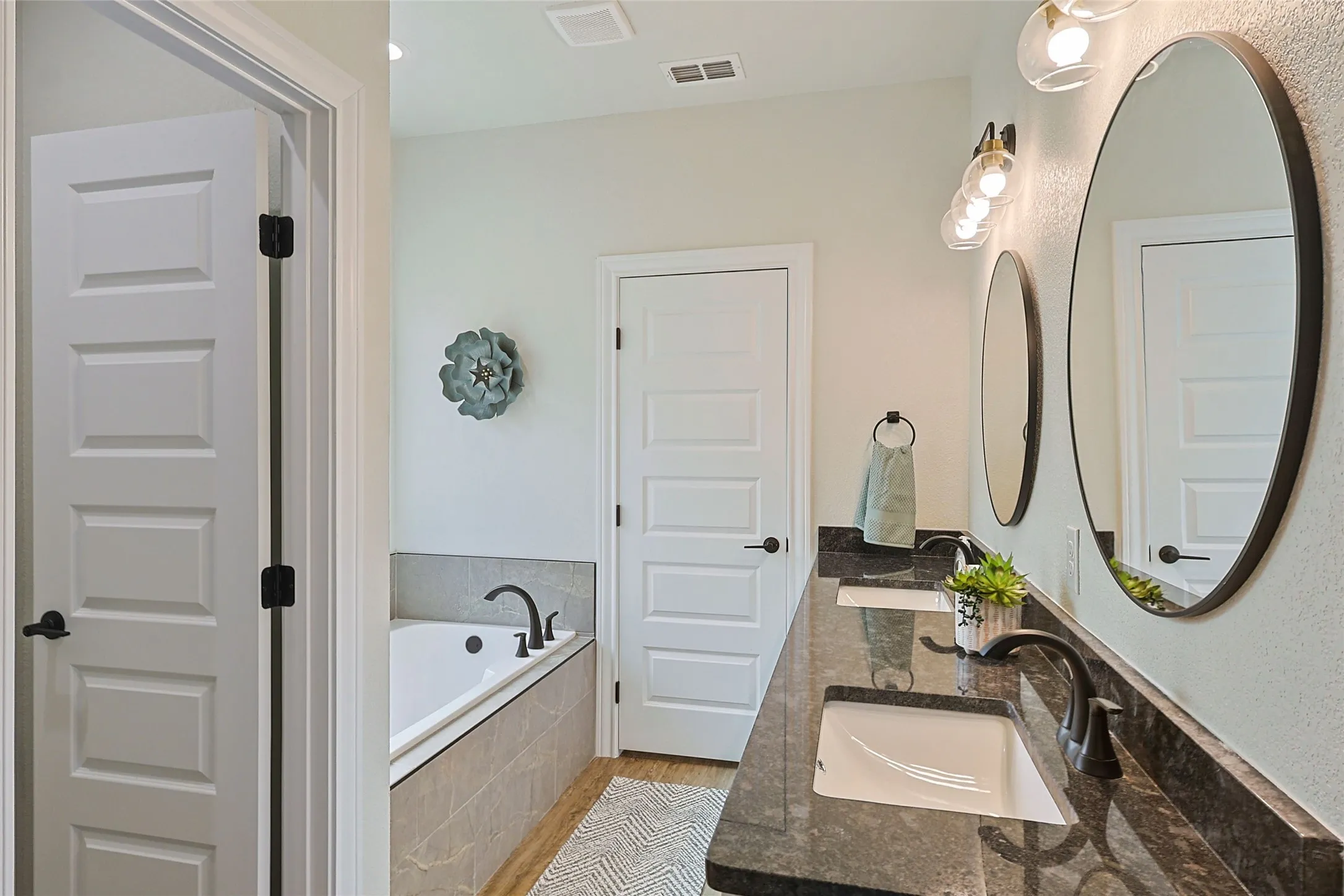 Dual vanity with dark granite countertops and undermount sinks, illuminated by a three-light fixture