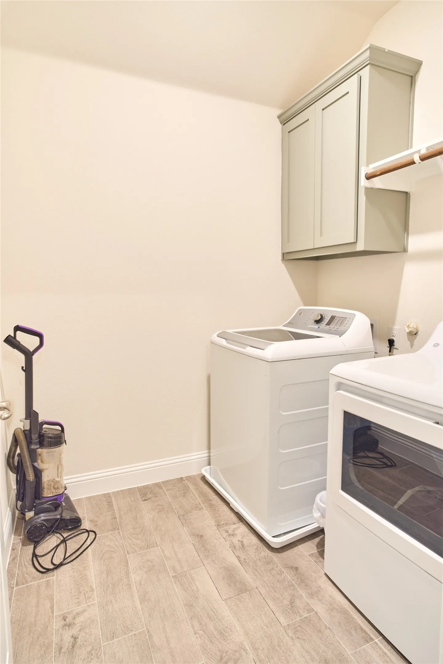 Dedicated utility space featuring wood-finish tile flooring, a wall-mounted storage cabinet, and a functional hanging rod