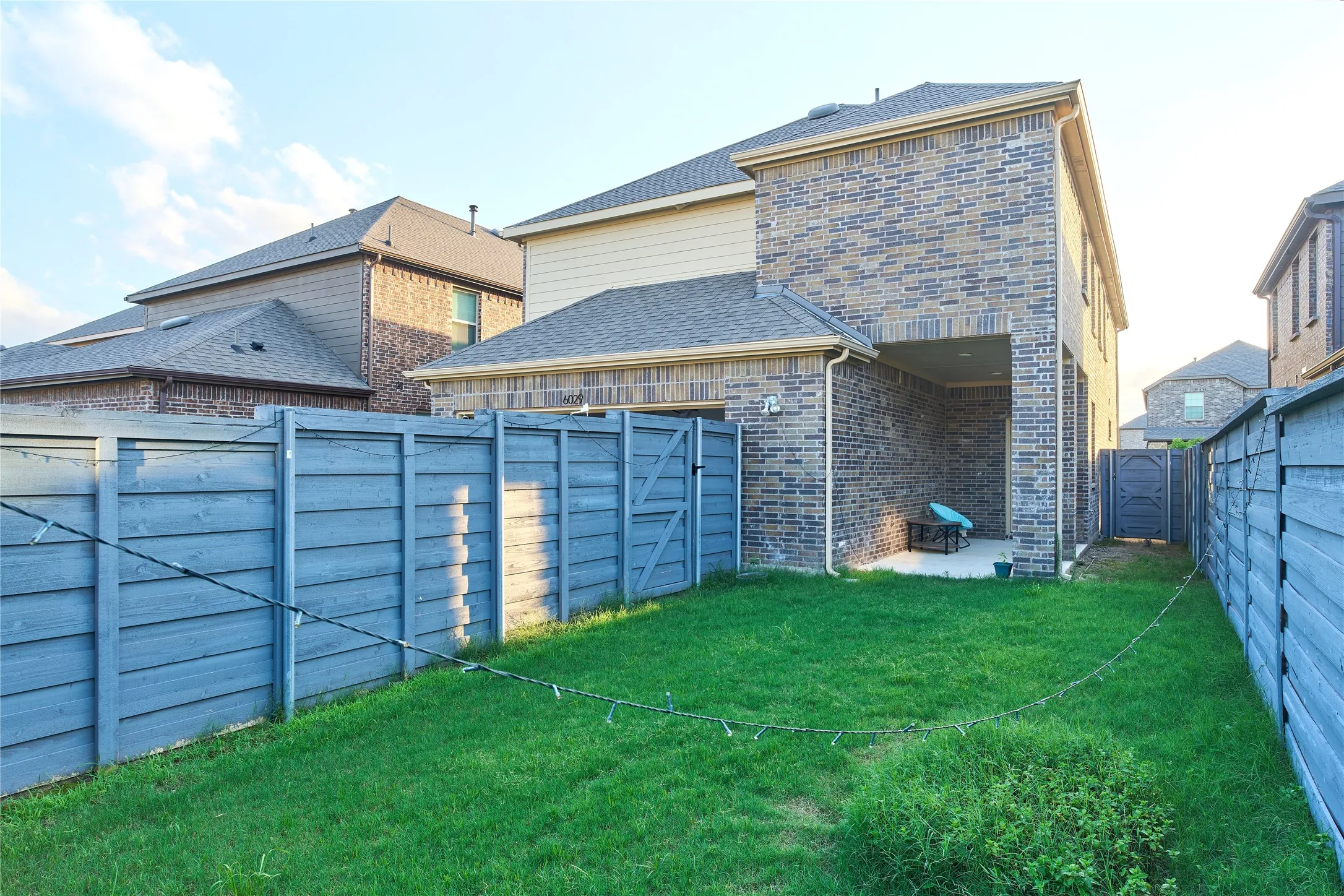 Fenced backyard featuring a covered patio, brick exterior, and a side gate access