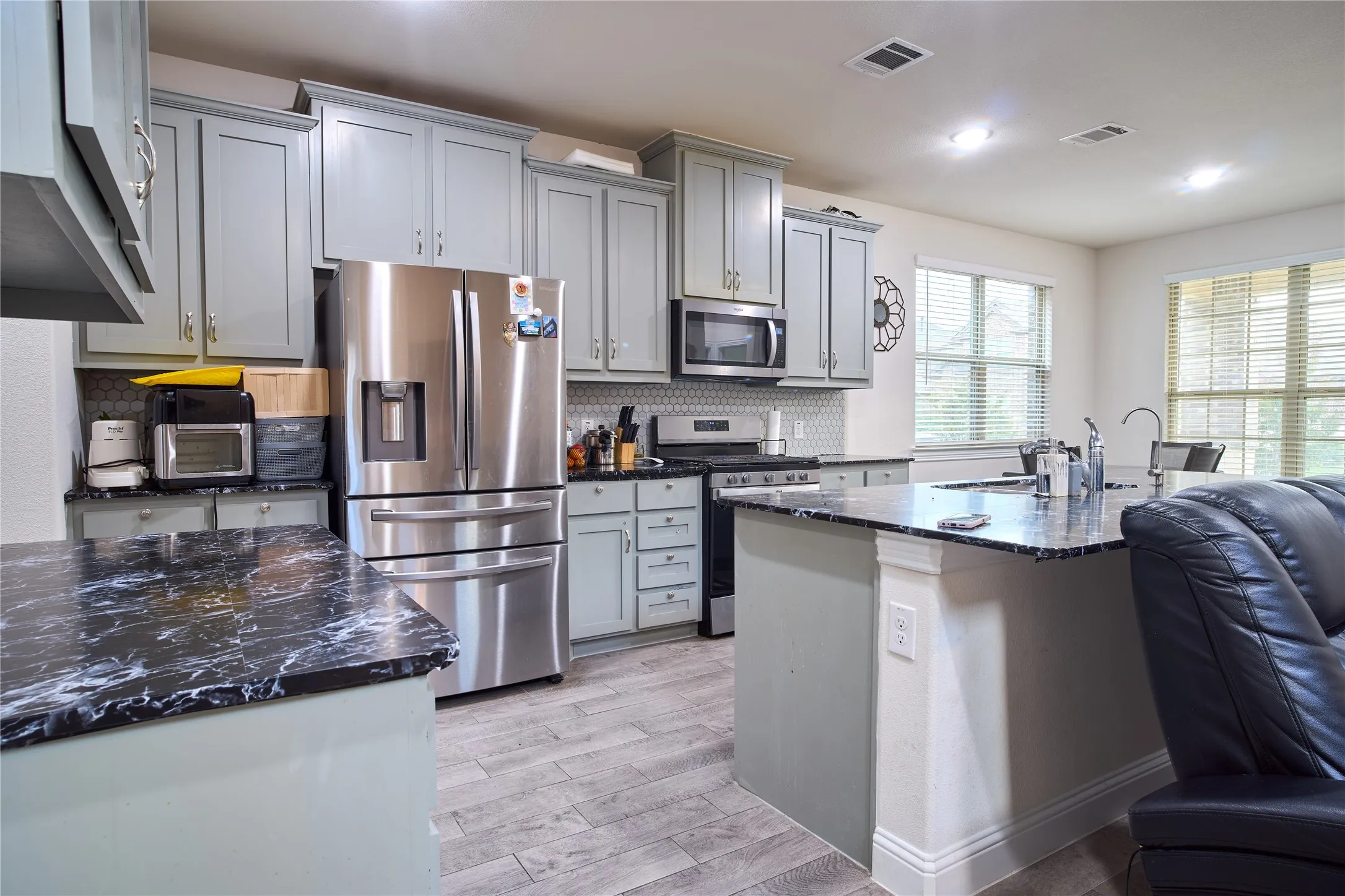 Kitchen with light gray cabinetry, dark marbled countertops, stainless steel appliances, and wood-finish flooring