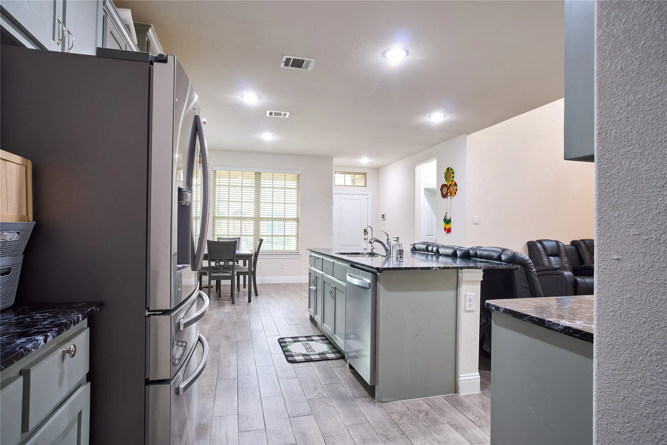 Kitchen featuring an island with a built-in sink, dark countertops, and light gray cabinetry