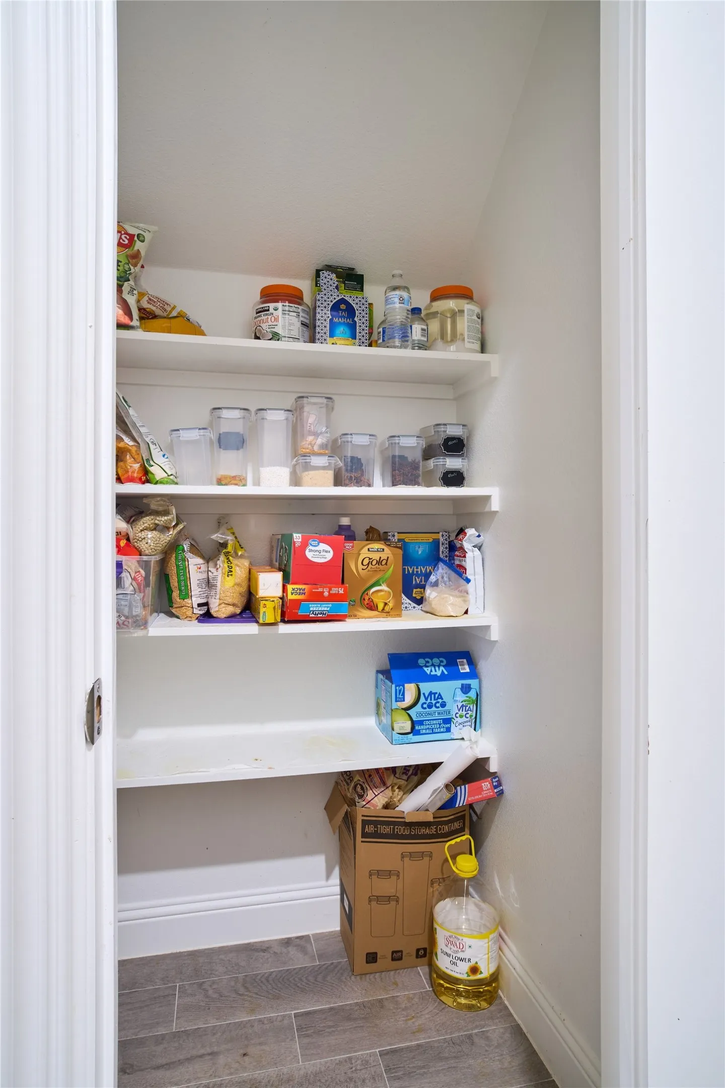 Pantry featuring white built-in shelving, white baseboards, and grey wood-finish tile flooring