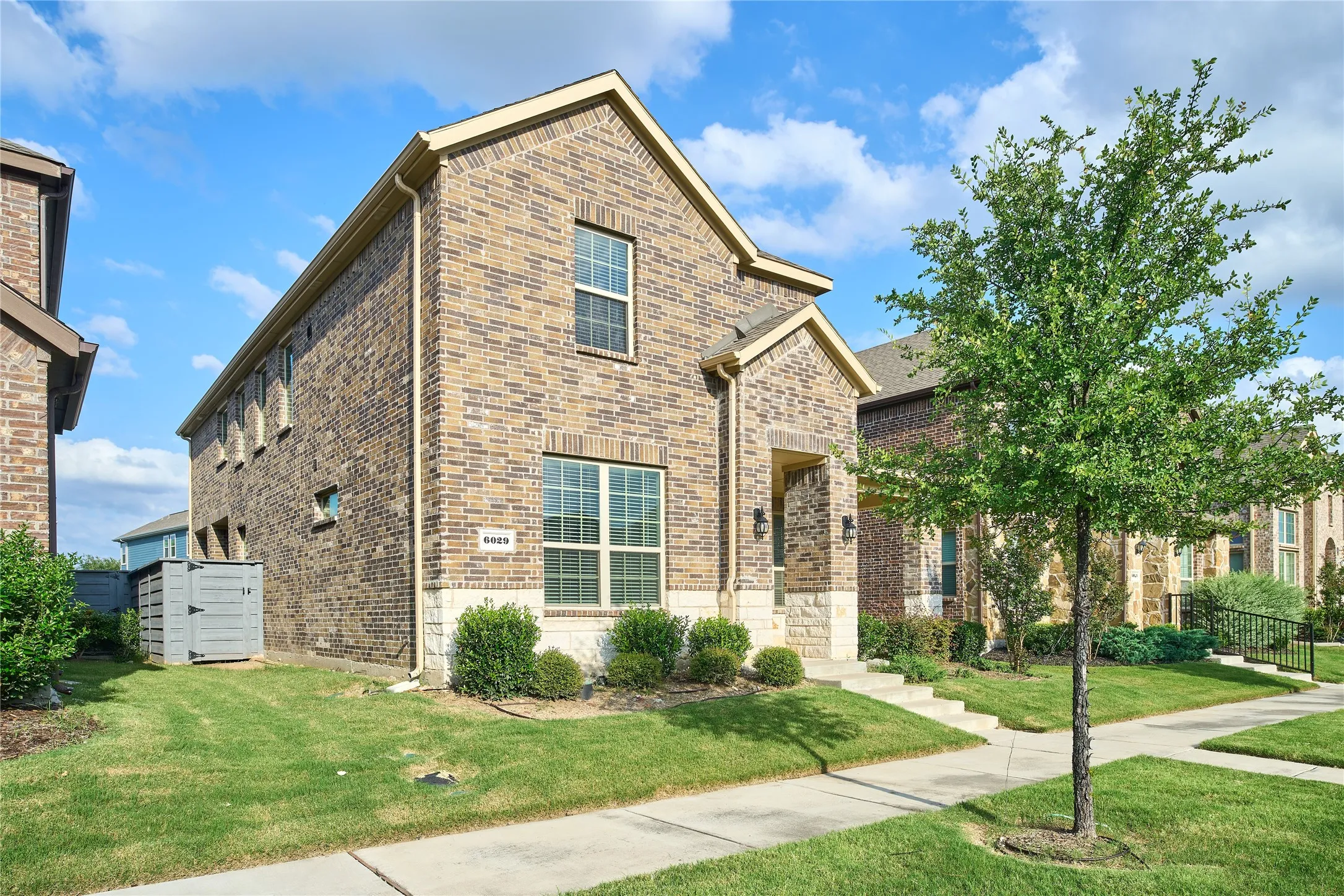 Brick and stone-front home featuring a covered entry, gabled roofline, and established landscaping