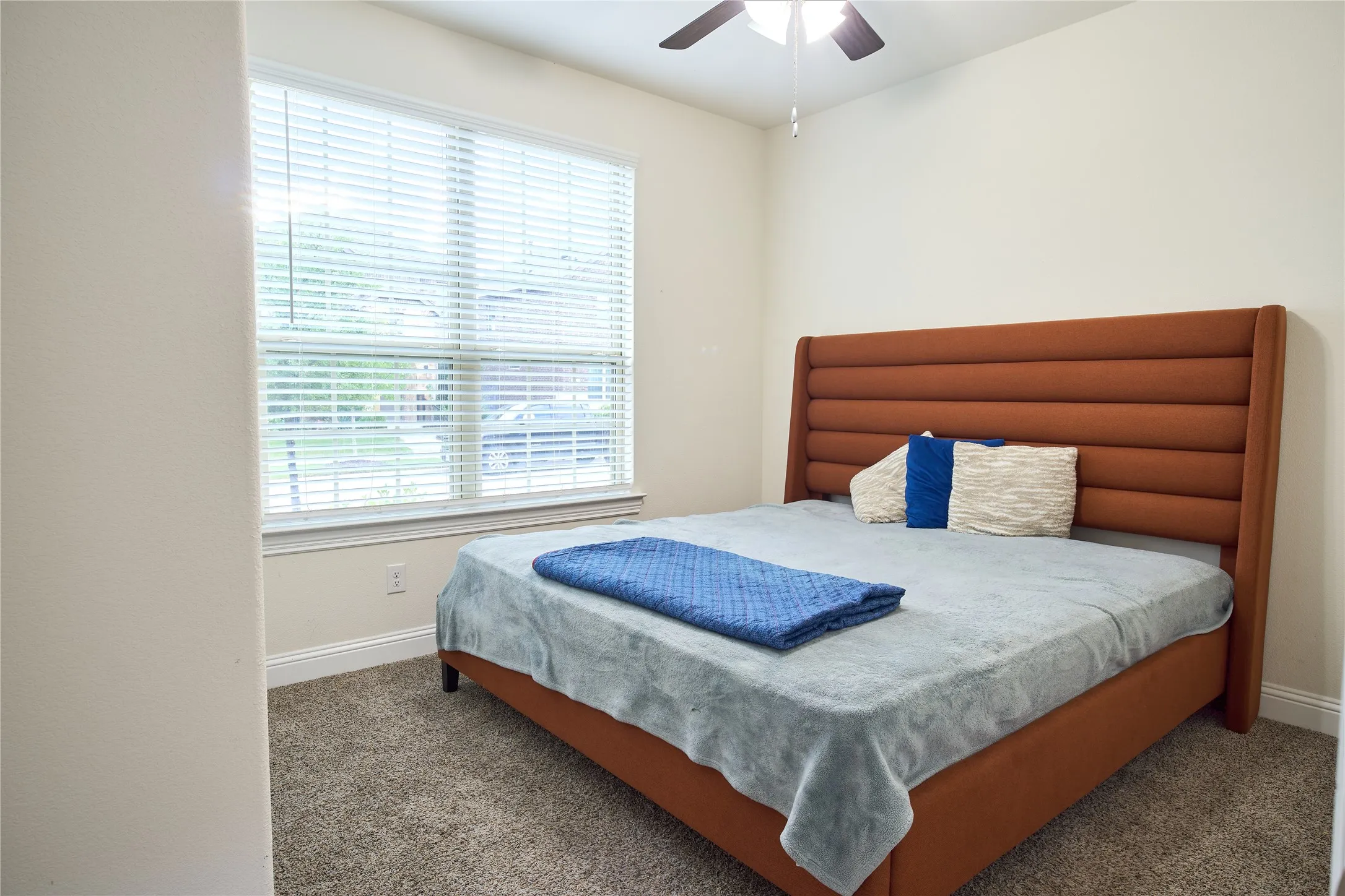 Carpeted room featuring a large window with blinds, ceiling fan, and painted walls with baseboard trim