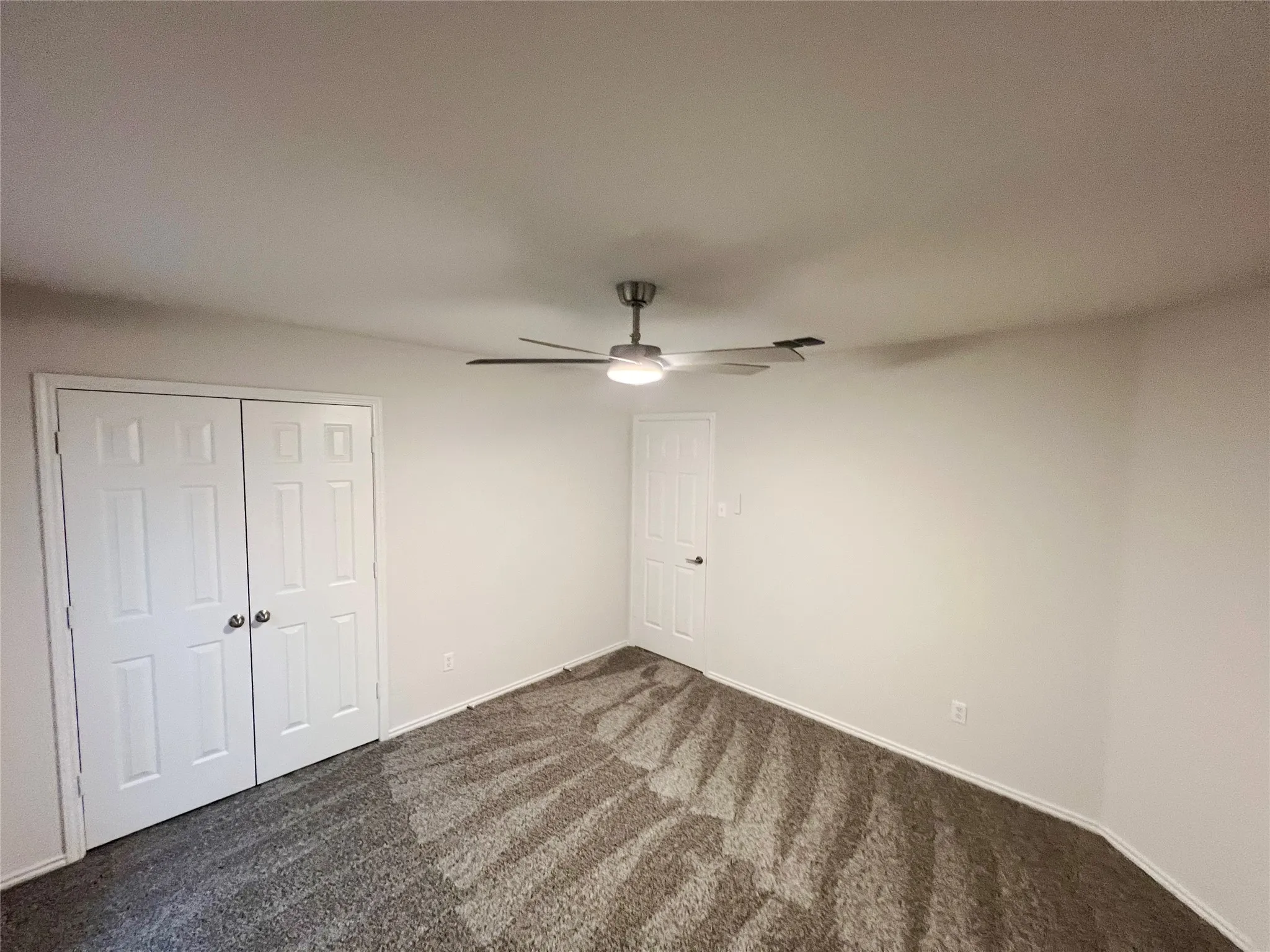 Interior room featuring white walls, a ceiling fan with integrated lighting, and textured grey carpeting