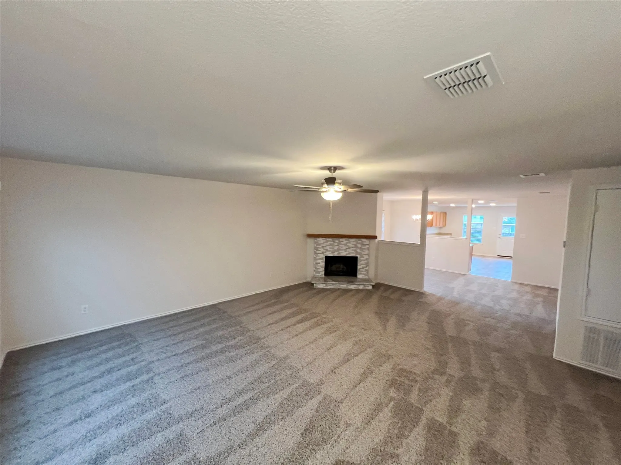 Spacious living area featuring patterned carpeting and a corner fireplace with stone surround and wood mantle