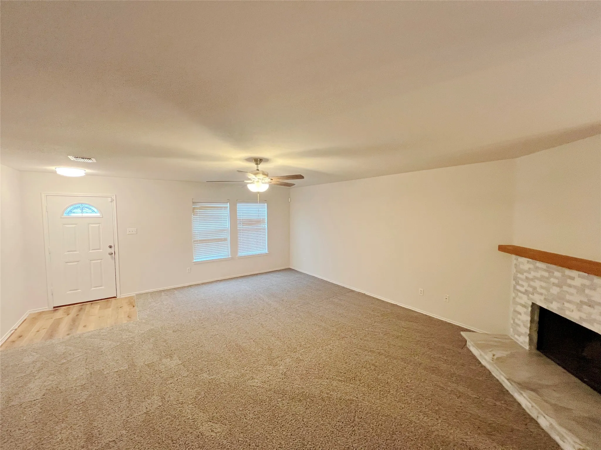 Spacious living area featuring neutral carpeting and a decorative fireplace with a light-toned brick surround and wood mantel