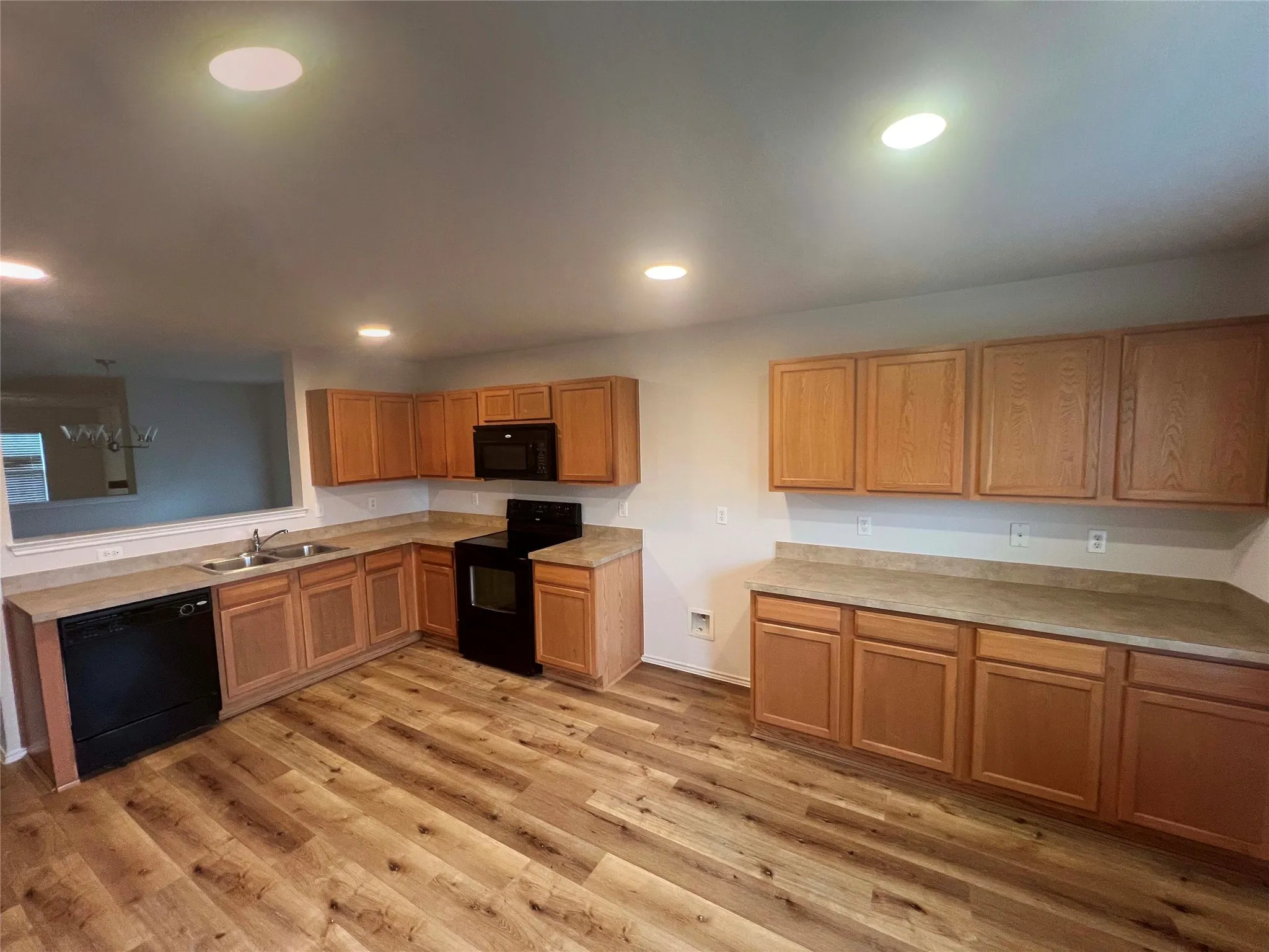 Spacious kitchen featuring wood-finish flooring, extensive cabinetry, a double basin sink, black appliances, and recessed lighting