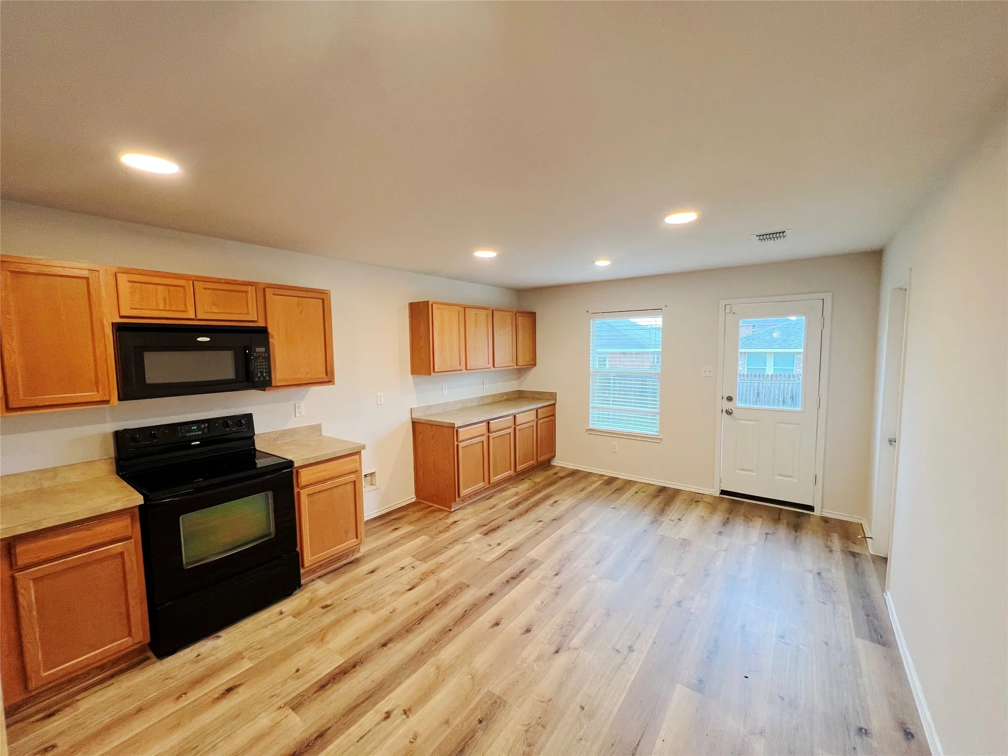 Open-concept kitchen area featuring wood-finish flooring, recessed lighting, wood cabinetry, built-in microwave, and a black electric range