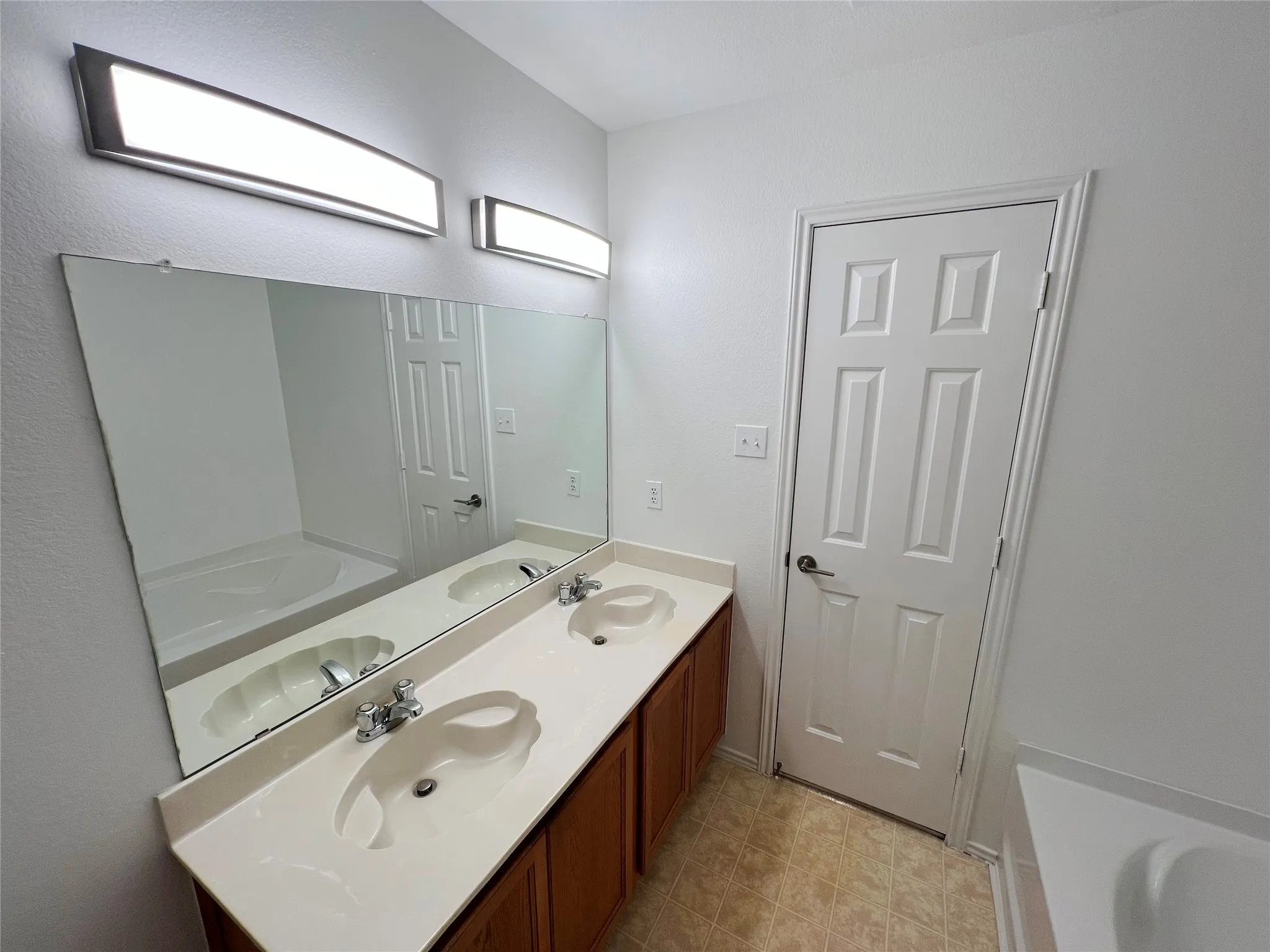 Bathroom featuring a dual vanity with integrated sinks, a large wall-mounted mirror, and contemporary linear light fixtures
