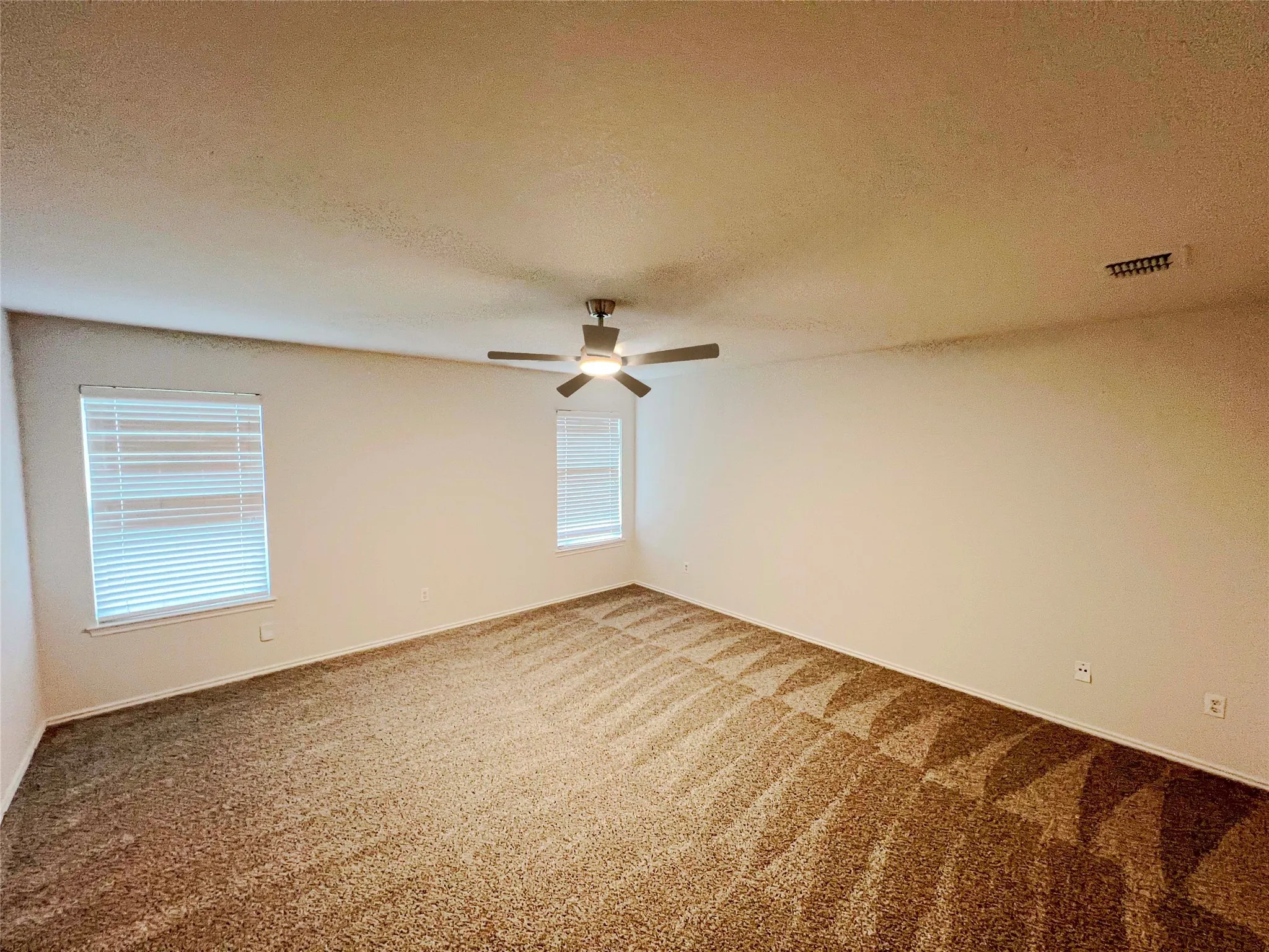Spacious carpeted room featuring a ceiling fan, two windows with blinds, and neutral wall tones