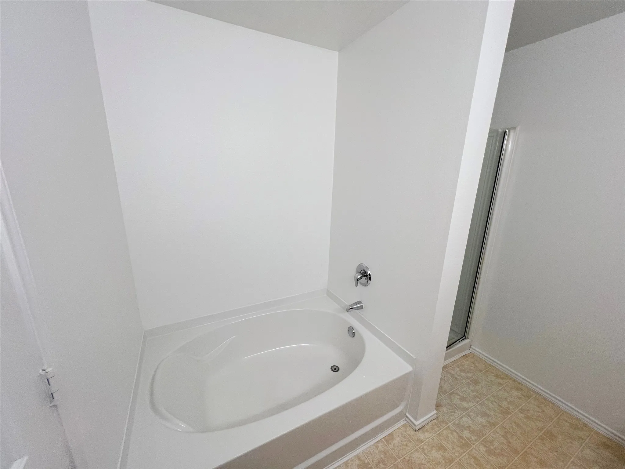 White drop-in bathtub with chrome fixtures and light-toned floor tiling