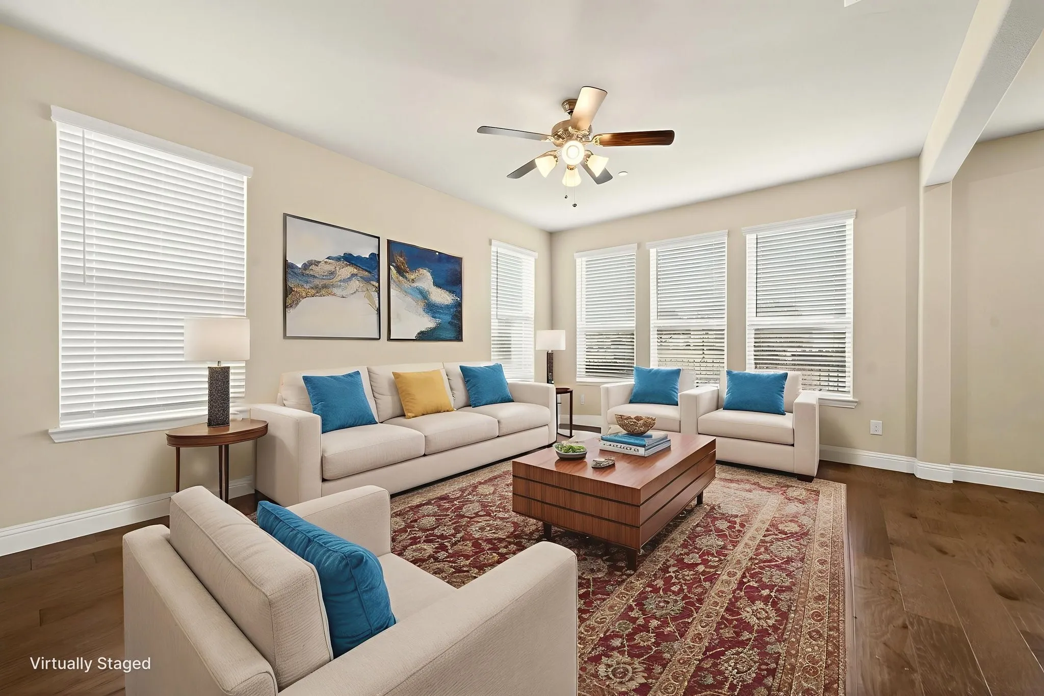 Spacious living area featuring rich wood-finish flooring, multiple windows with blinds, a ceiling fan with integrated lighting, and neutral wall tones