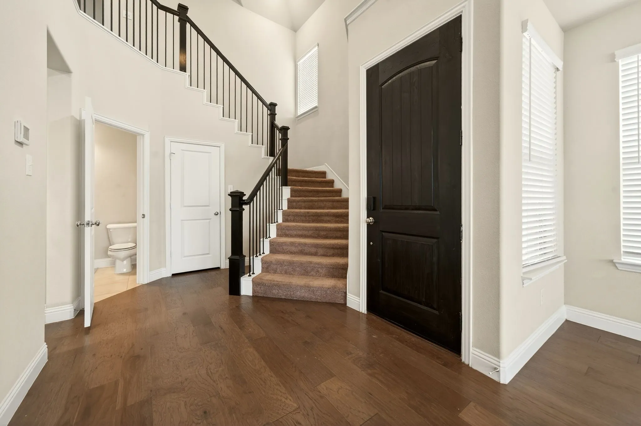 Entry foyer featuring wood-finish flooring, a dark wood-finish entry door, and a carpeted staircase with dark wood-finish railings