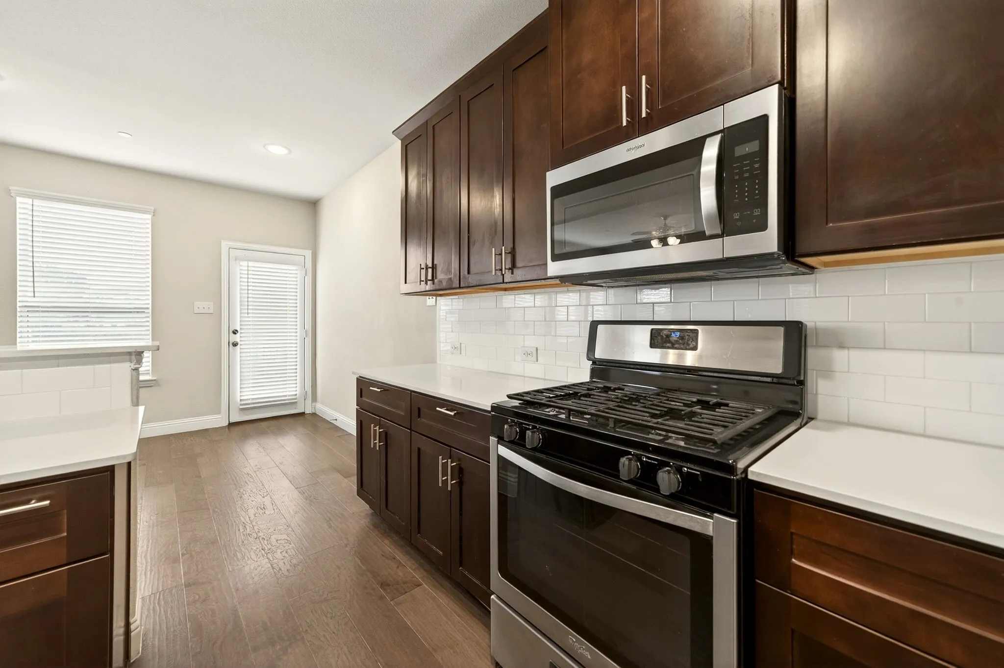 Kitchen featuring dark wood cabinetry, stainless steel range with overhead microwave, white subway tile backsplash, light-toned countertops, and wood-finish flooring