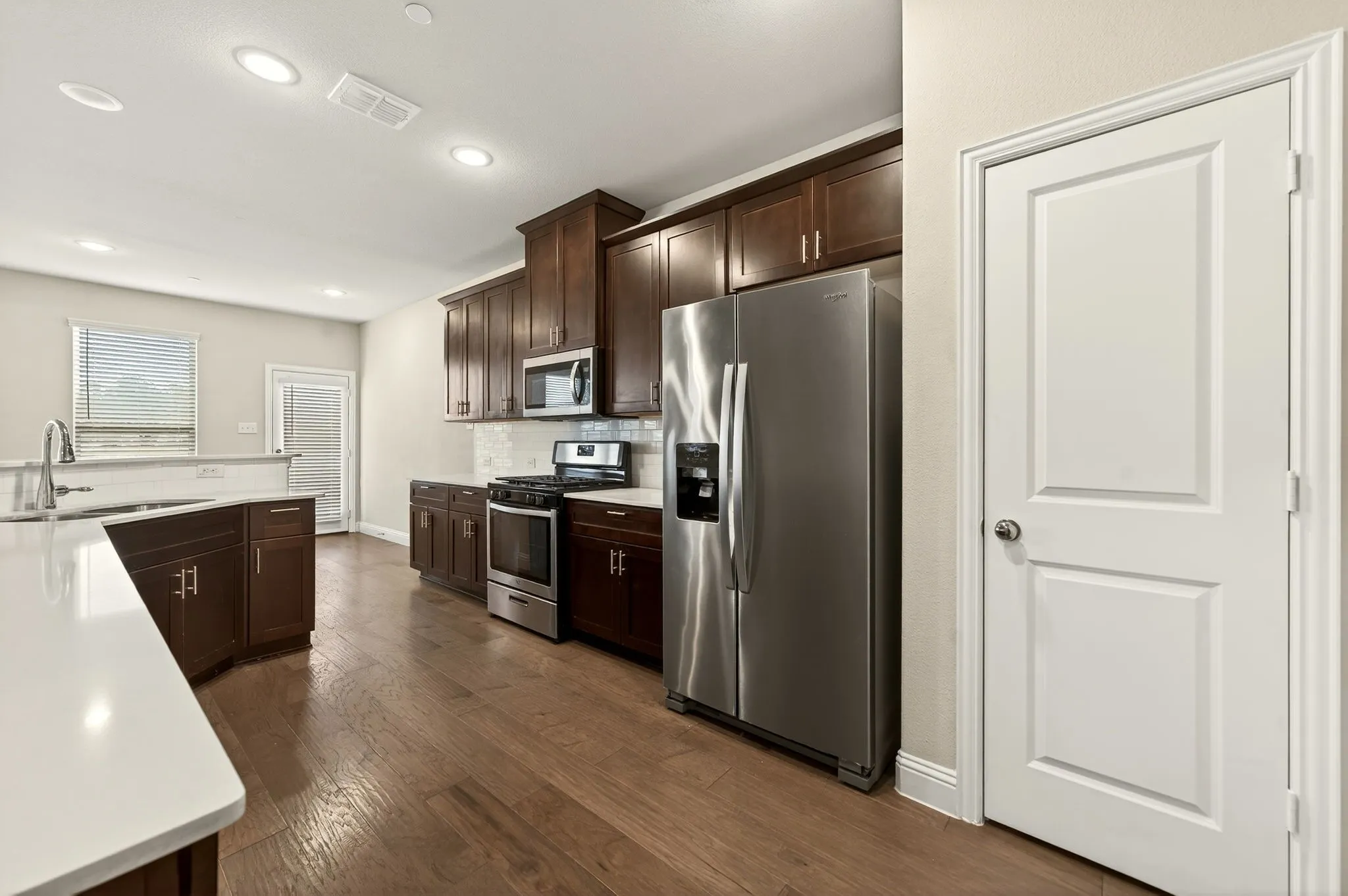 Modern kitchen featuring wood-finish flooring, dark wood cabinetry, white countertops, and stainless steel appliances