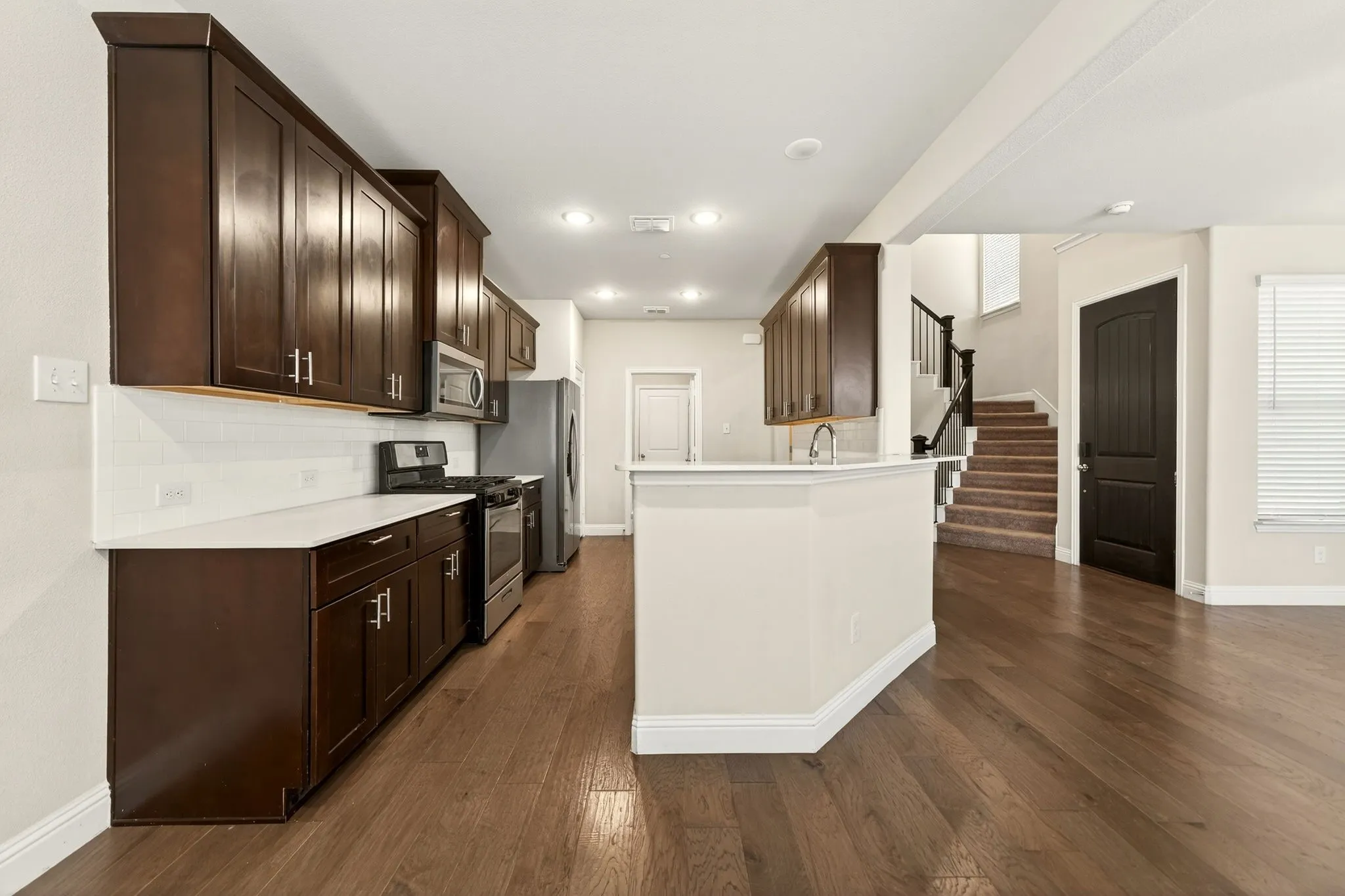 Kitchen featuring dark wood cabinetry, white countertops, stainless steel appliances, and a subway tile backsplash