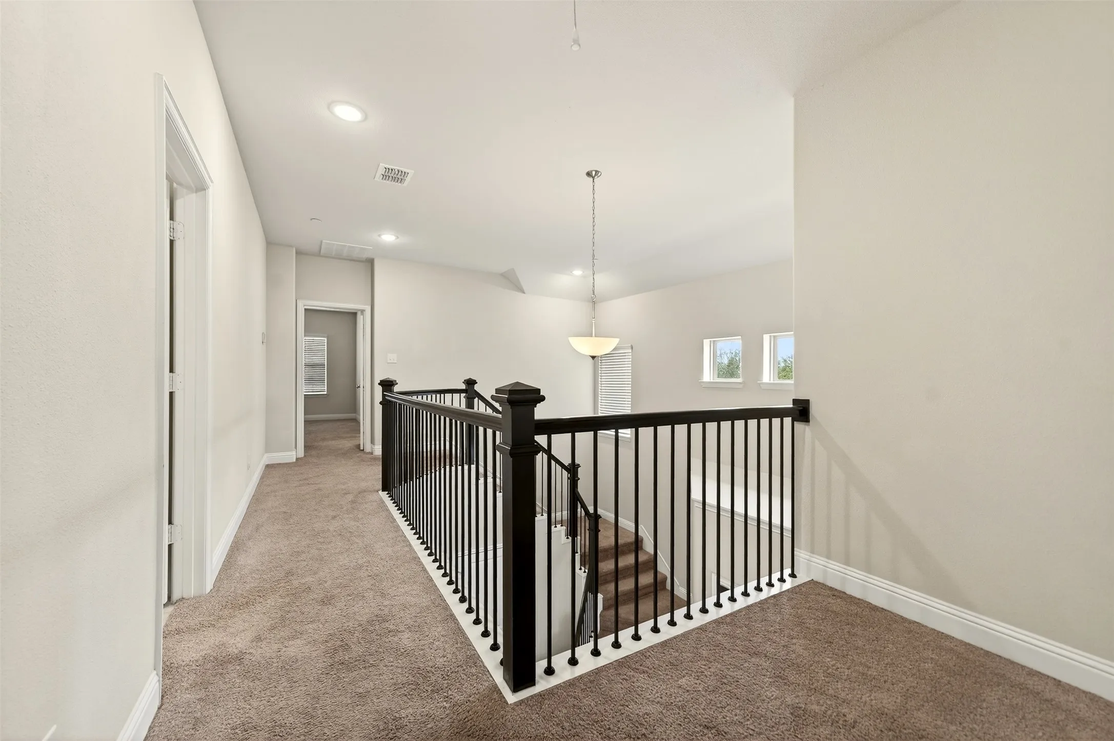Upper landing featuring a black wrought iron balustrade, carpet flooring, recessed lighting, and a pendant light fixture