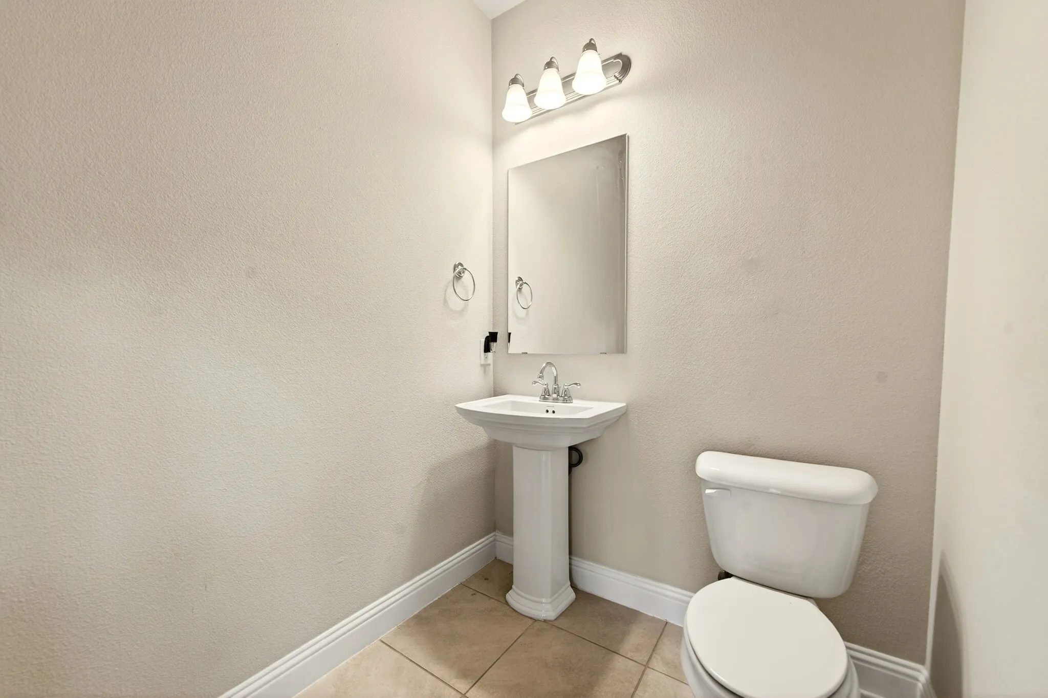 Bathroom featuring a pedestal sink, wall-mounted mirror, three-light vanity fixture, and tiled flooring