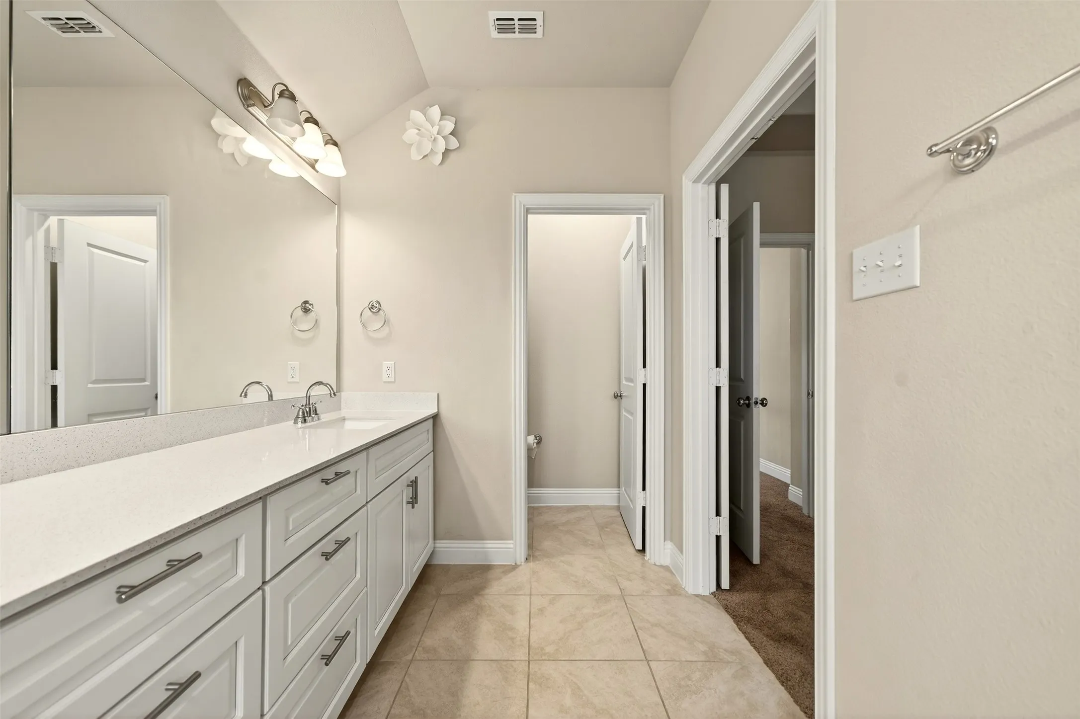 Primary bathroom with double vanity with white cabinetry, brushed nickel hardware, and a light-toned countertop