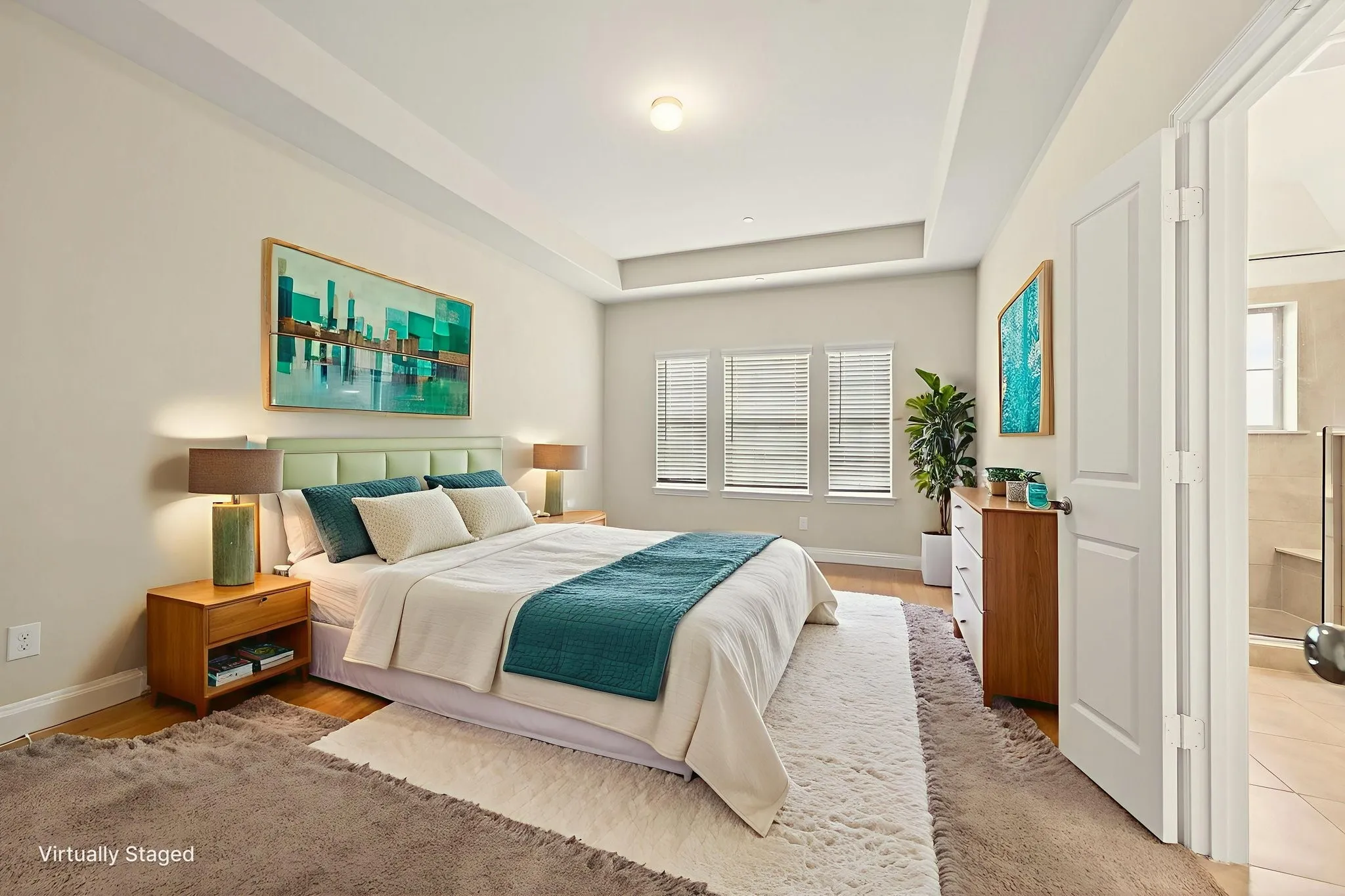 Virtually staged primary bedroom featuring a tray ceiling, three windows with blinds, an upholstered headboard, and a doorway leading to a tiled bathroom