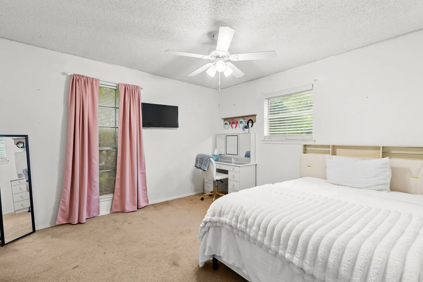 Carpeted bedroom featuring a ceiling fan, two windows with blinds, and white painted walls