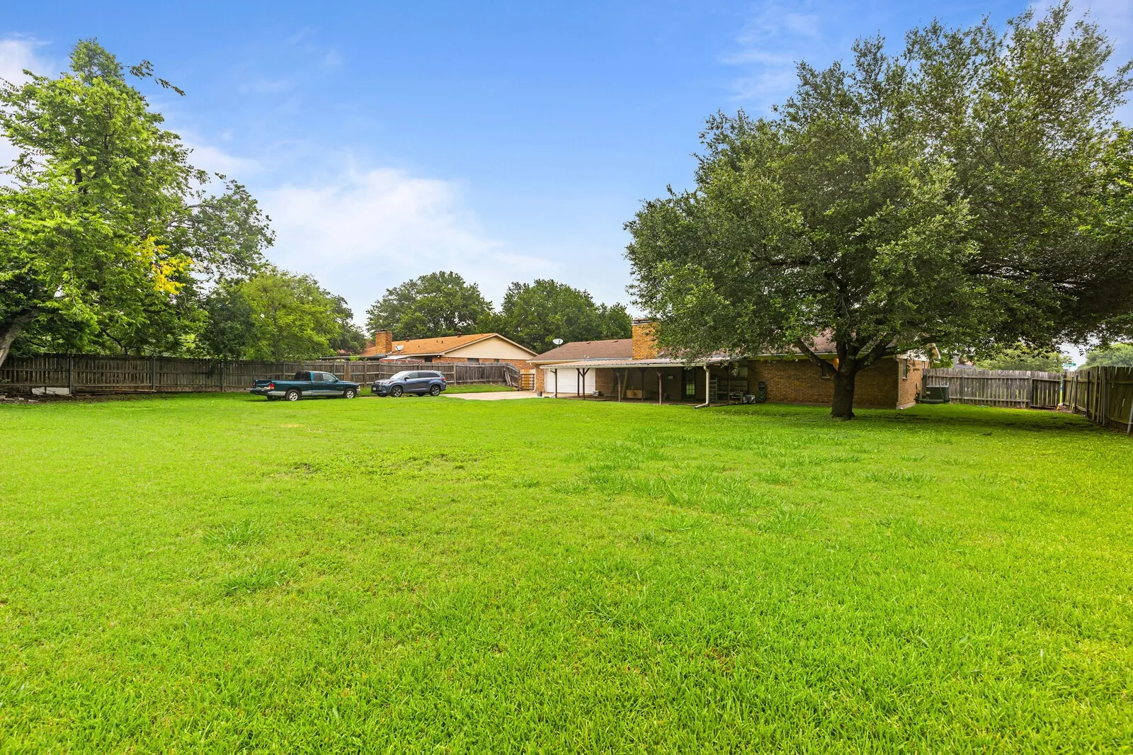 Expansive backyard featuring a lush green lawn, mature shade trees, and privacy fencing