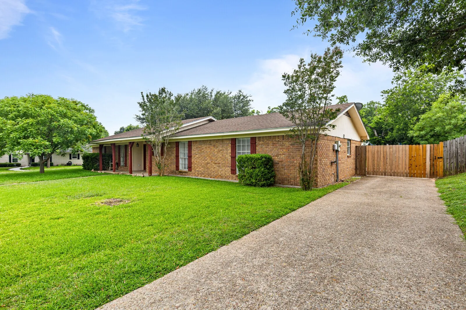 Brick exterior residence featuring a covered front porch, concrete driveway, and a wood privacy fence