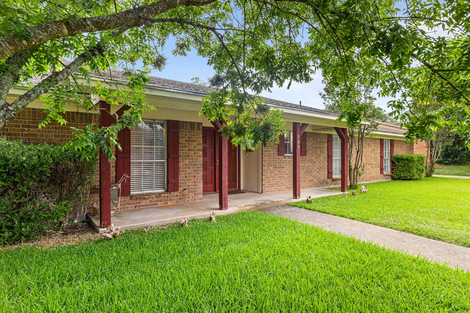 Brick exterior with a covered front porch, red accent shutters, and a concrete walkway