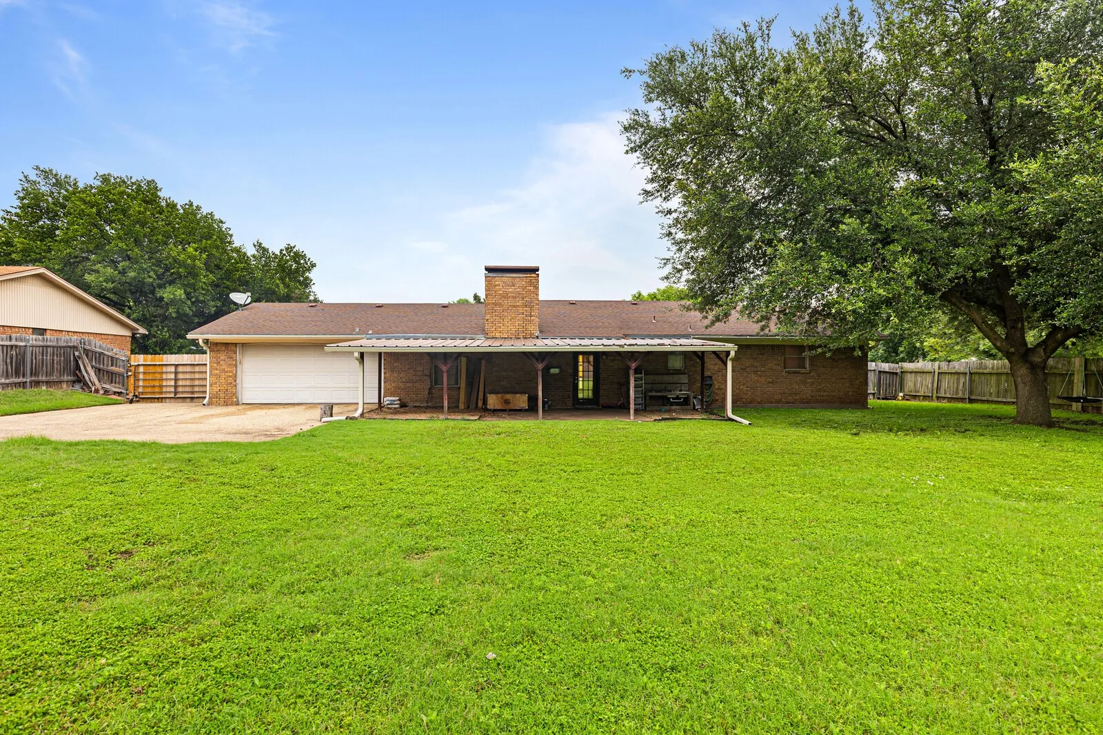 Expansive backyard featuring a large green lawn, mature shade tree, and wood privacy fencing