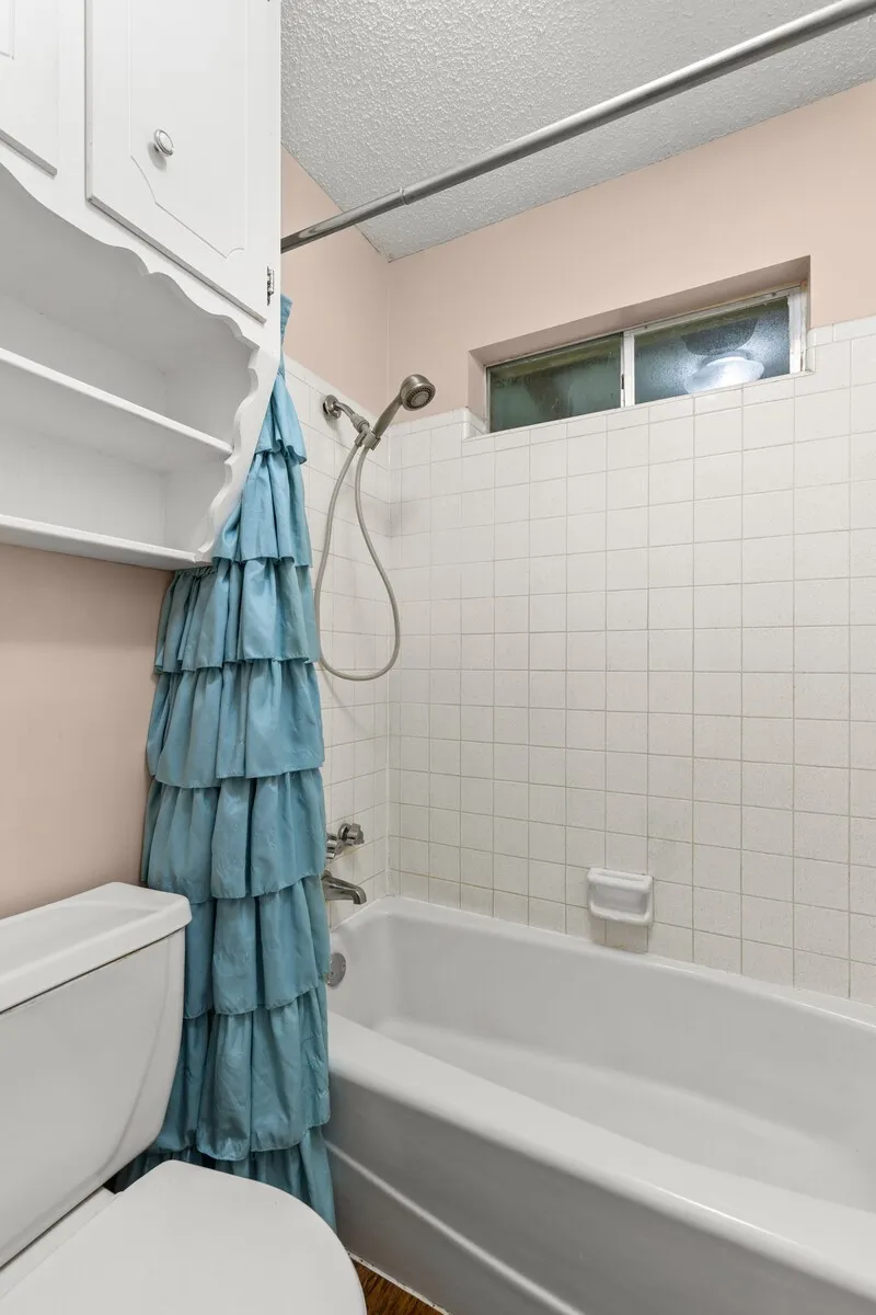 Bathroom featuring a white porcelain bathtub, white square wall tile, and a handheld shower fixture