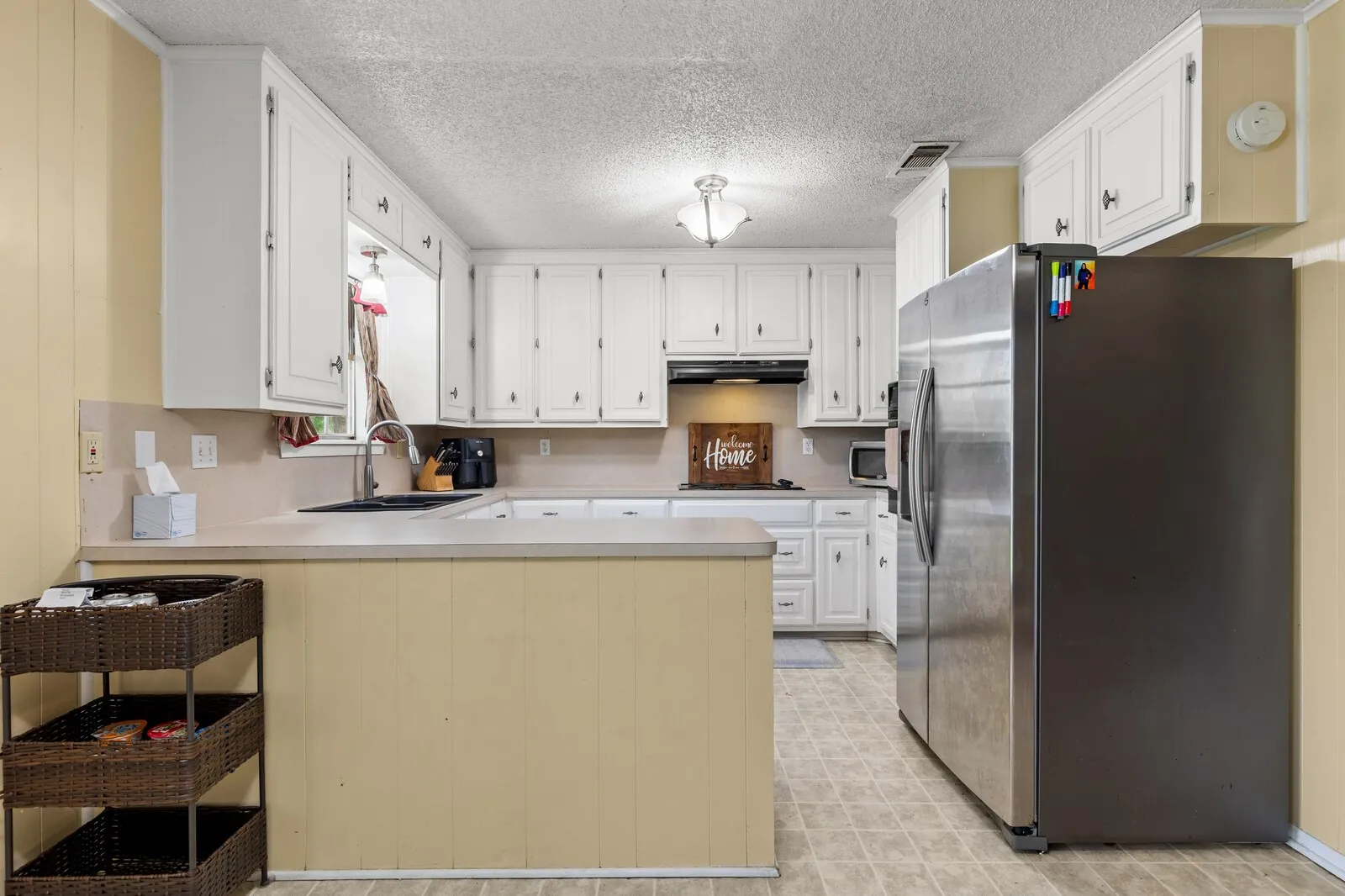 Kitchen featuring extensive white cabinetry, light-toned countertops, and a full-size stainless steel refrigerator