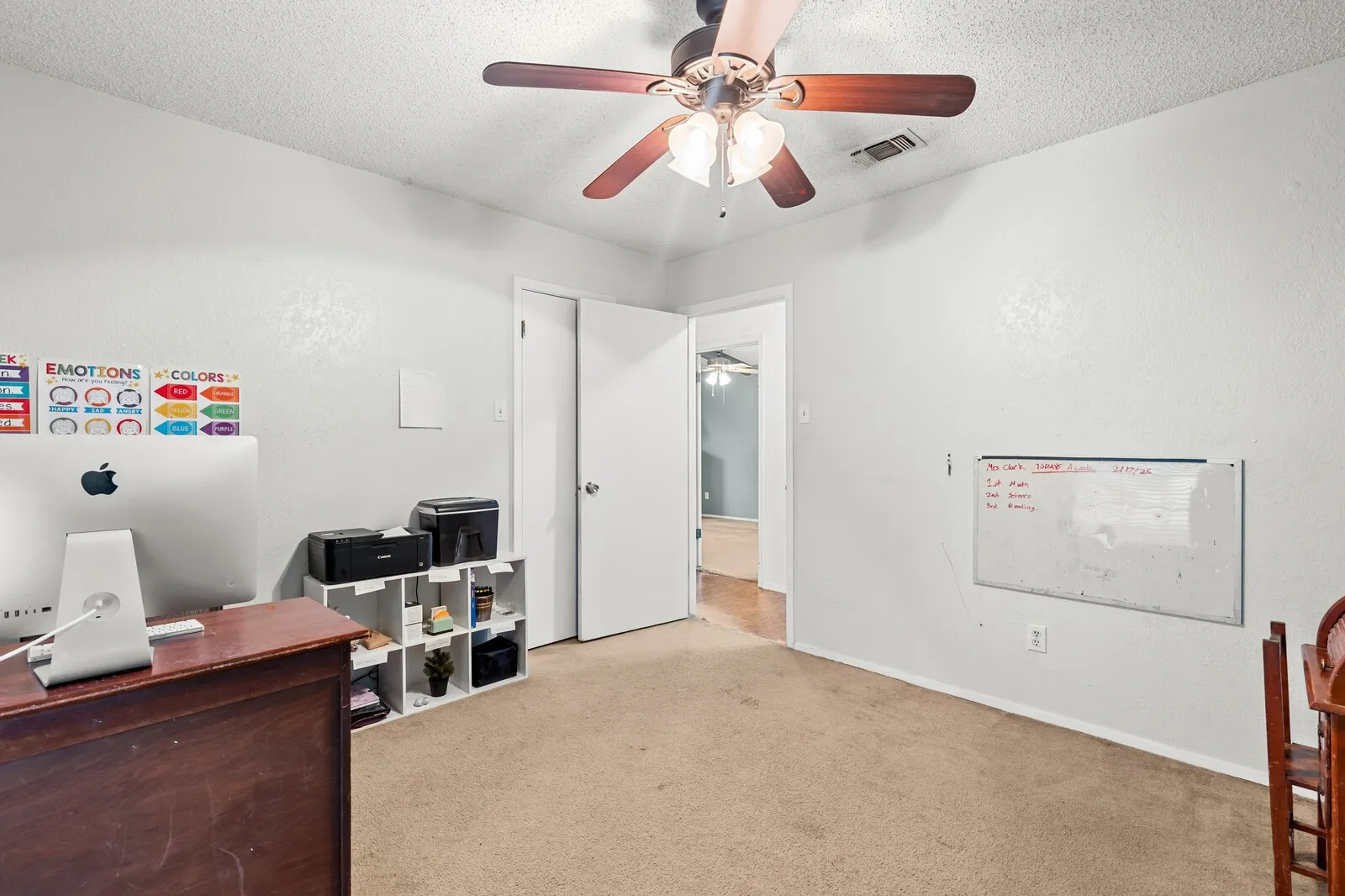 Carpeted room featuring a ceiling fan with light fixture, white walls, and a doorway opening to an additional interior space