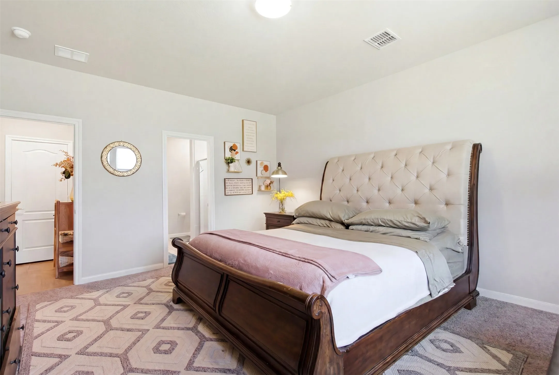 Spacious bedroom featuring light neutral wall paint, gray carpet flooring, and two doorways, one leading to a separate room and another to an en-suite bathroom with a shower