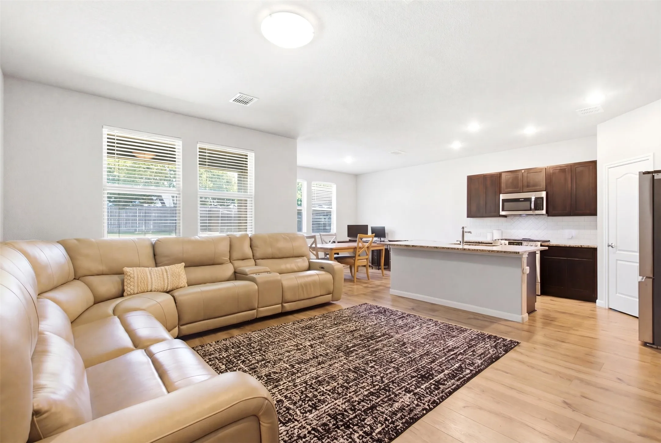 Open-concept living space featuring wood-finish flooring, recessed lighting, a kitchen island with a stone-look countertop, dark wood cabinetry, and a white subway tile backsplash