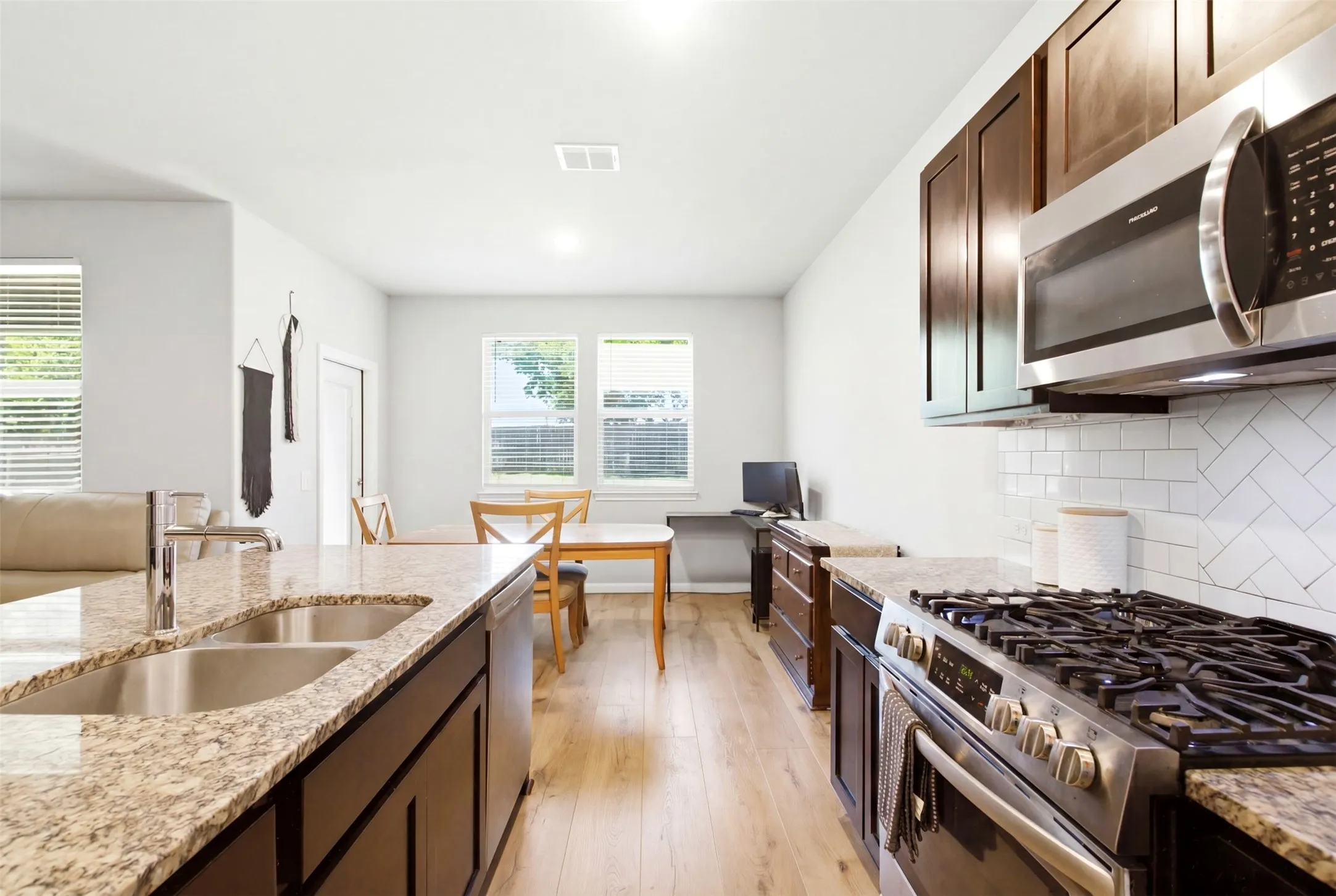 Modern kitchen featuring dark wood cabinetry, stainless steel appliances, speckled stone countertops, and a white subway tile backsplash