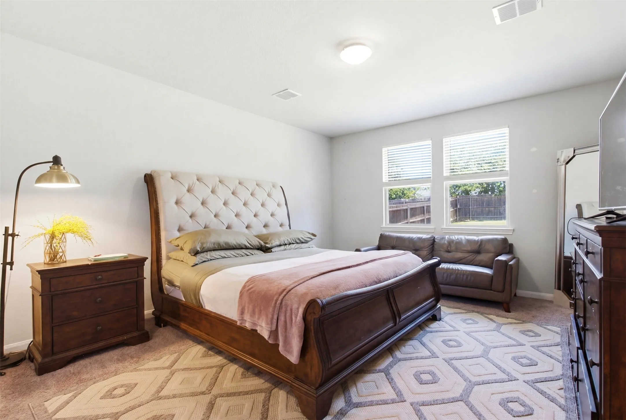 Spacious bedroom featuring light-colored walls, two windows with blinds, a ceiling light fixture, and carpeted flooring