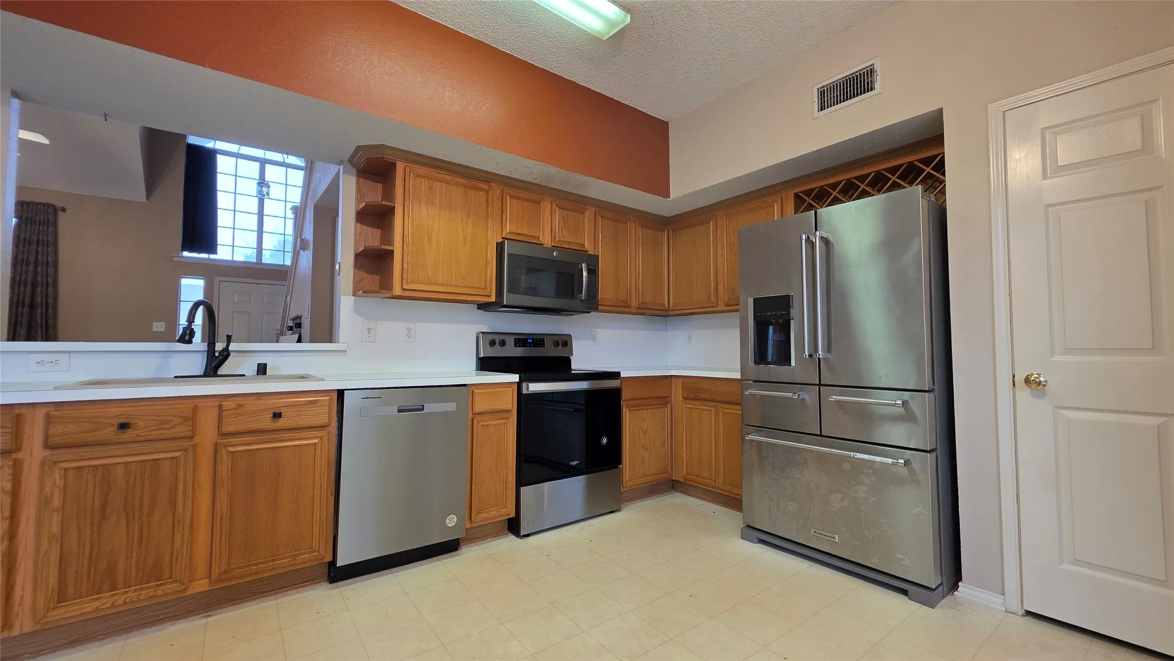 Kitchen featuring wood cabinetry, white countertops, black faucet, stainless steel appliances, and built-in wine storage