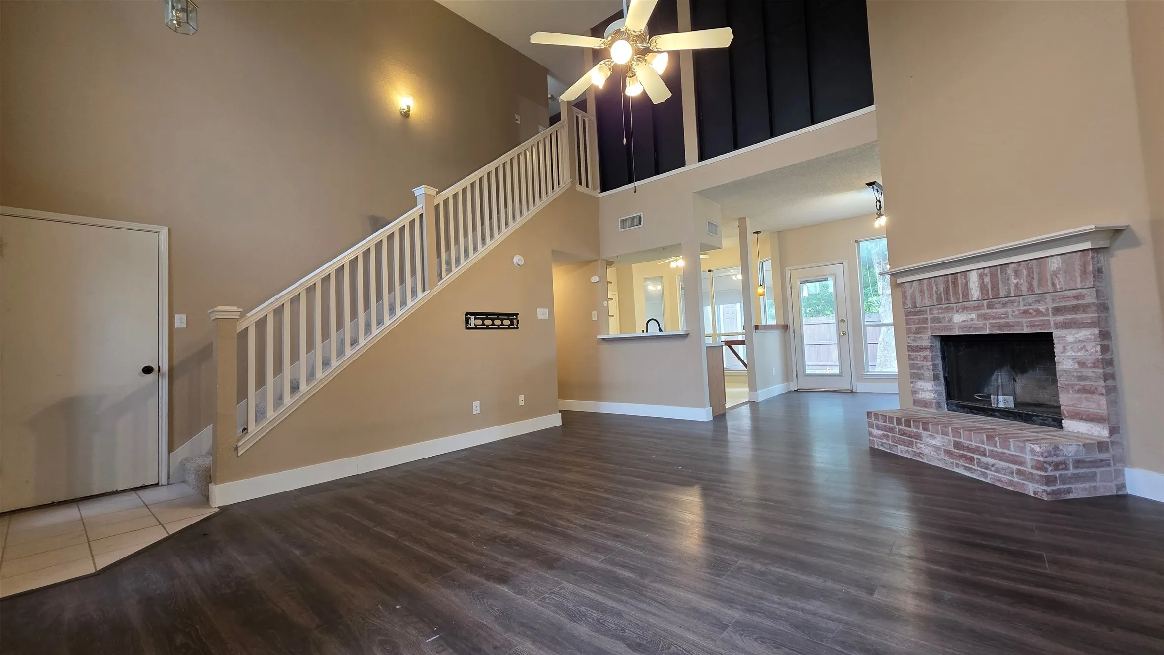 Spacious living area featuring high ceilings, wood-finish flooring, and a brick fireplace
