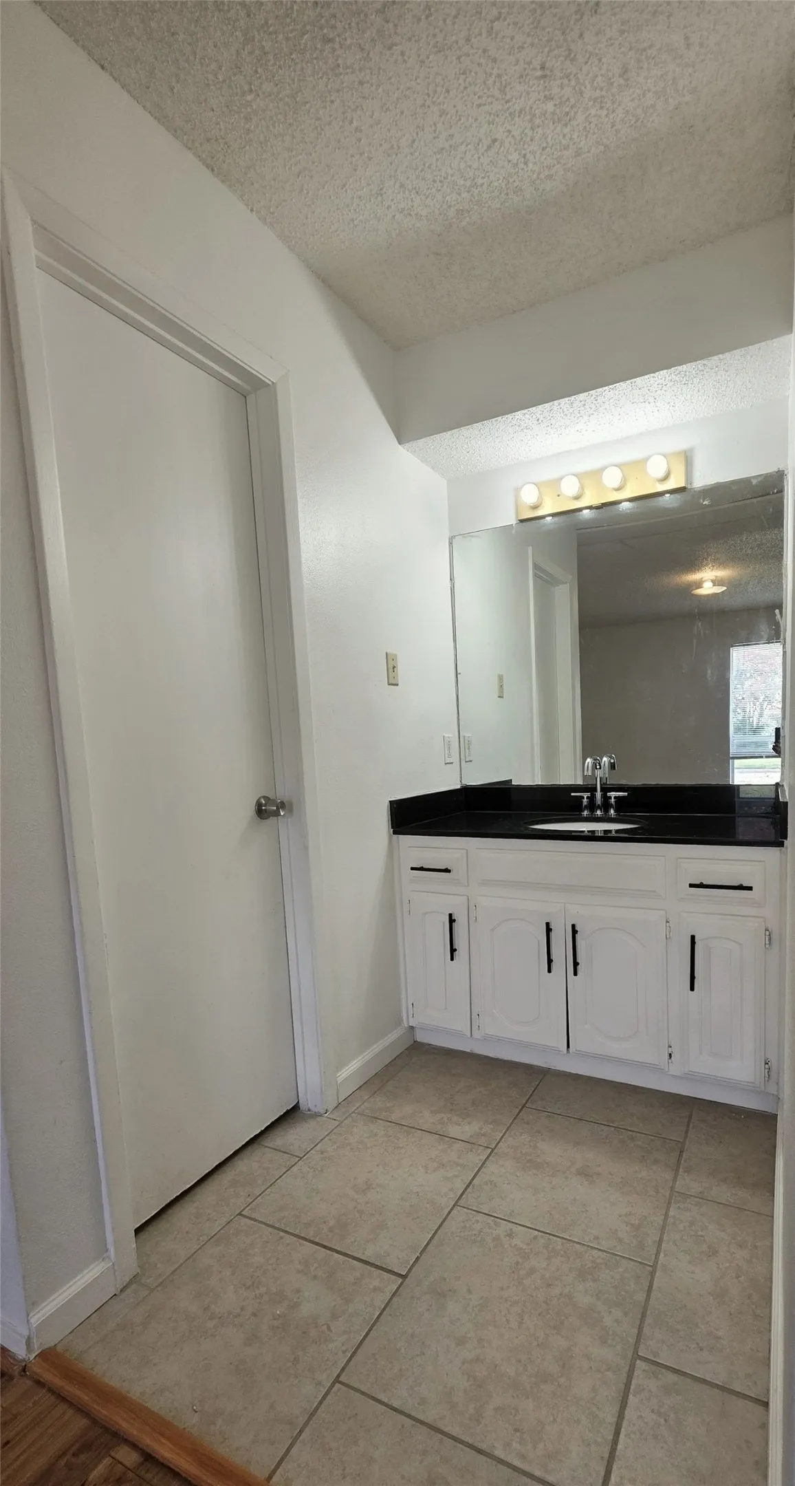 Vanity featuring a white cabinet with black hardware, a black countertop, and an integrated sink with a chrome faucet