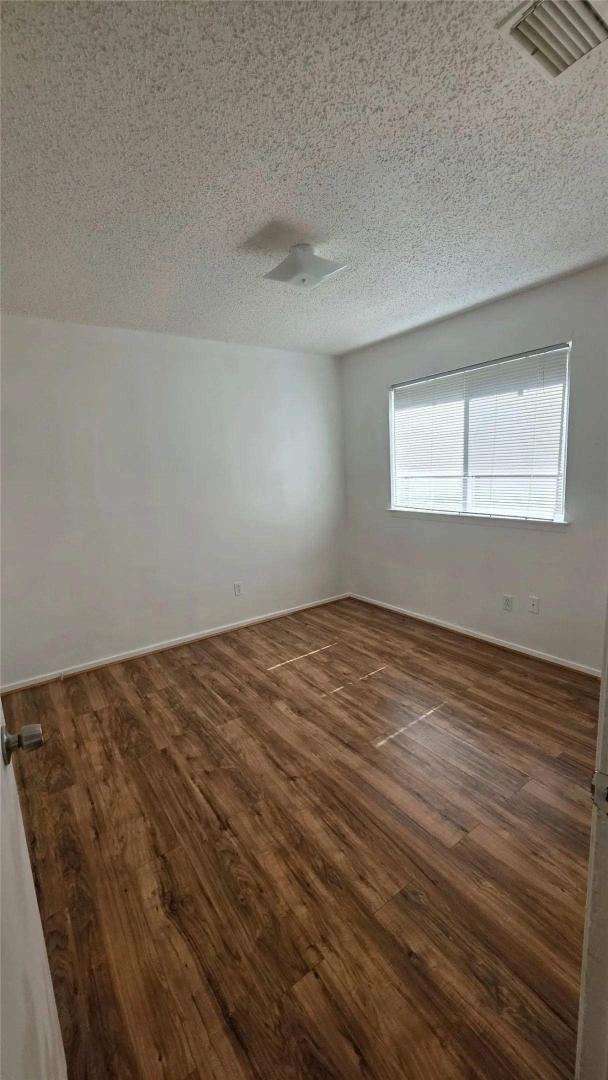 Spacious room featuring wood-finish flooring, white walls, and a window with horizontal blinds