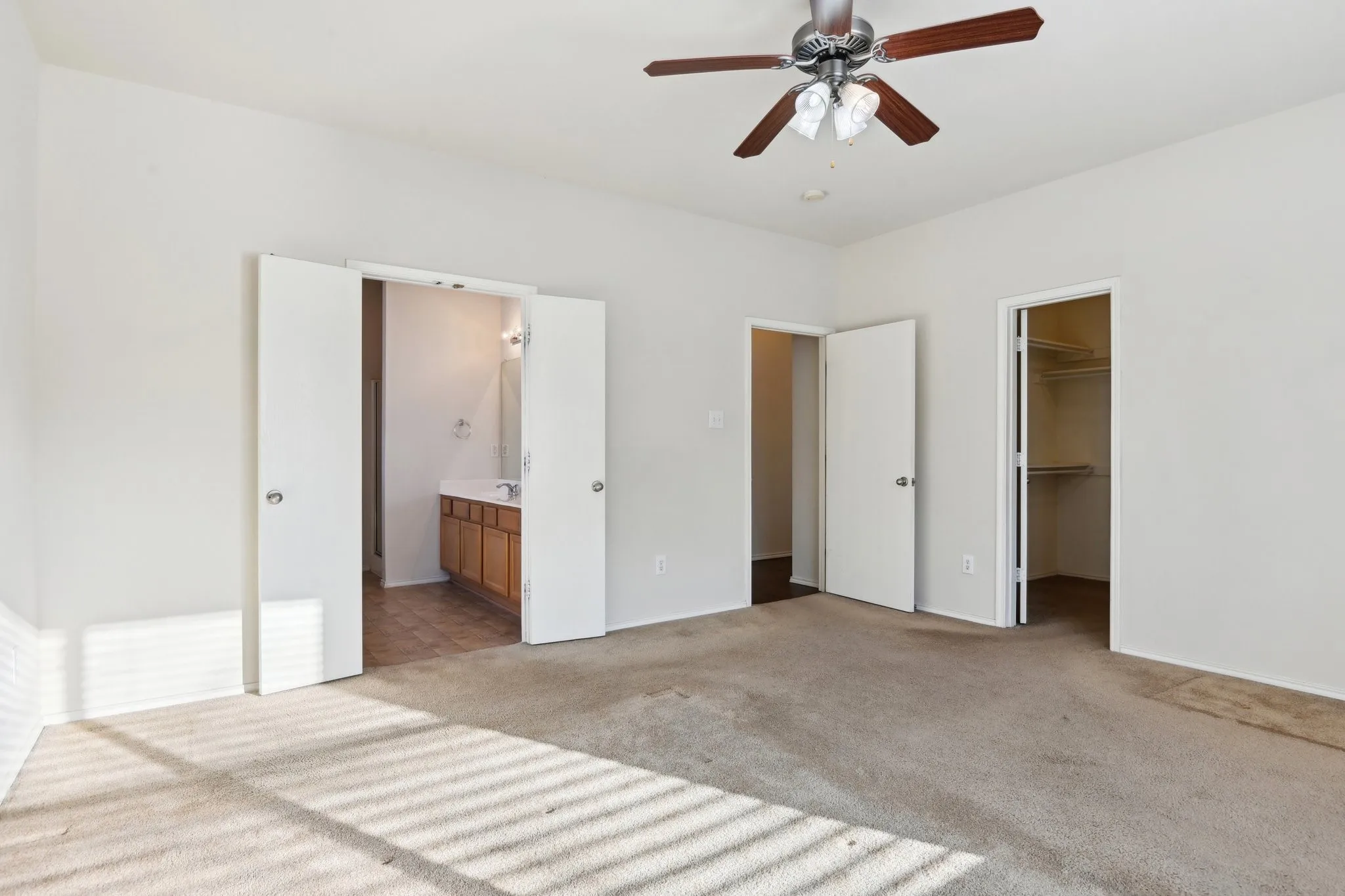 primary bedroom featuring ensuite bath, ceiling fan, light carpet, a walk in closet